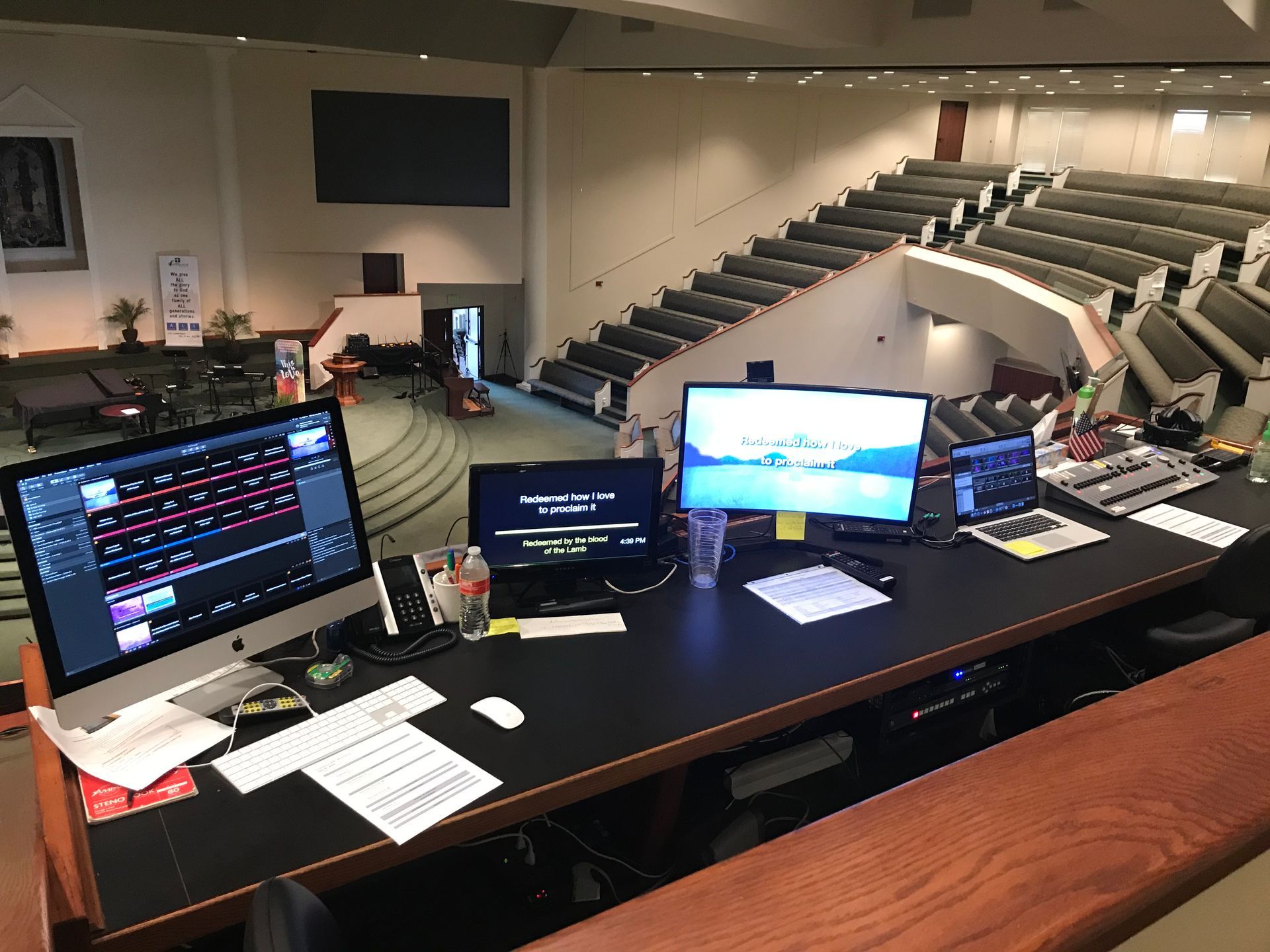 A desk with two computer monitors on it in a large auditorium.