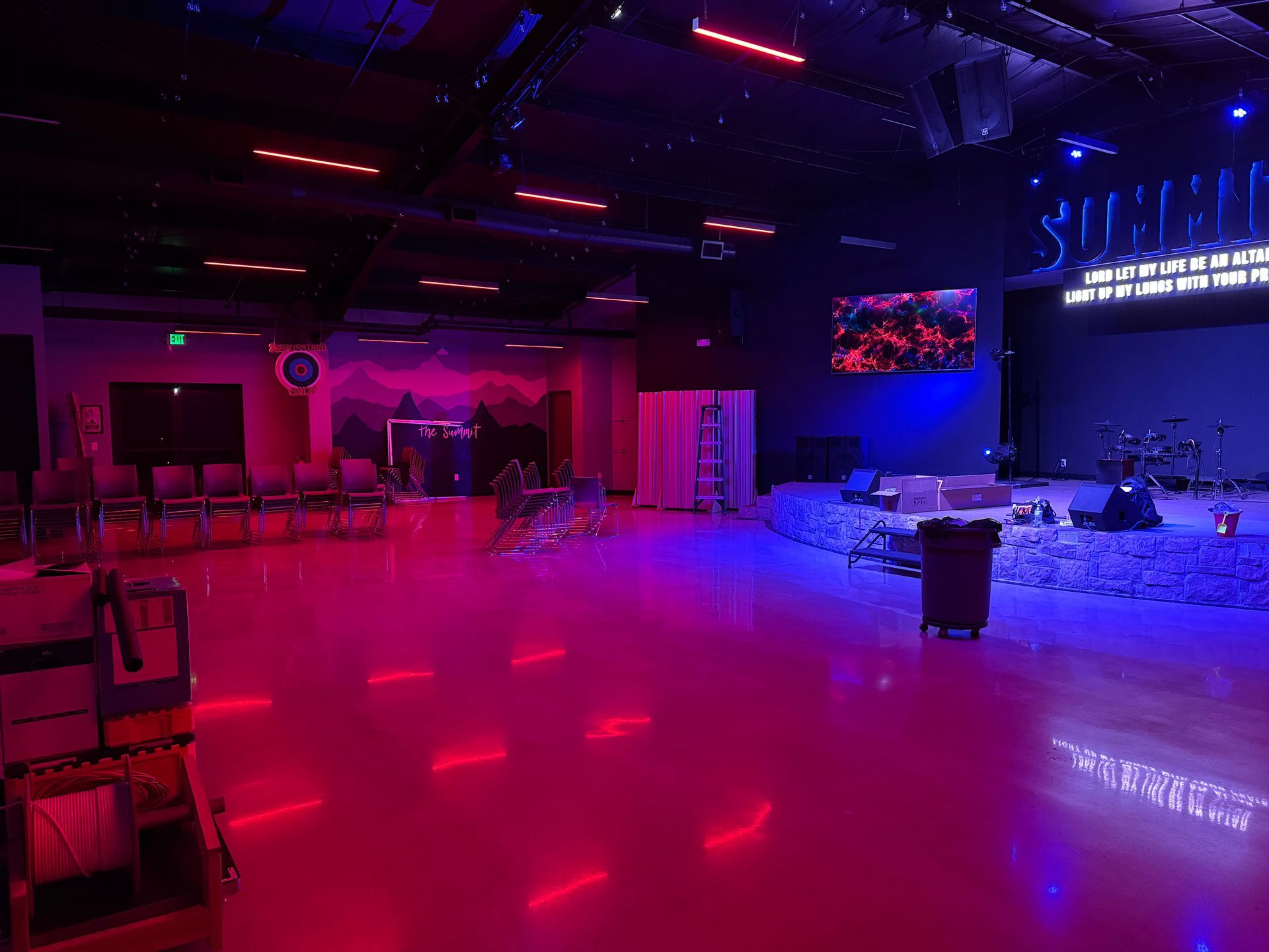 A large empty room with red and blue lights and a stage.