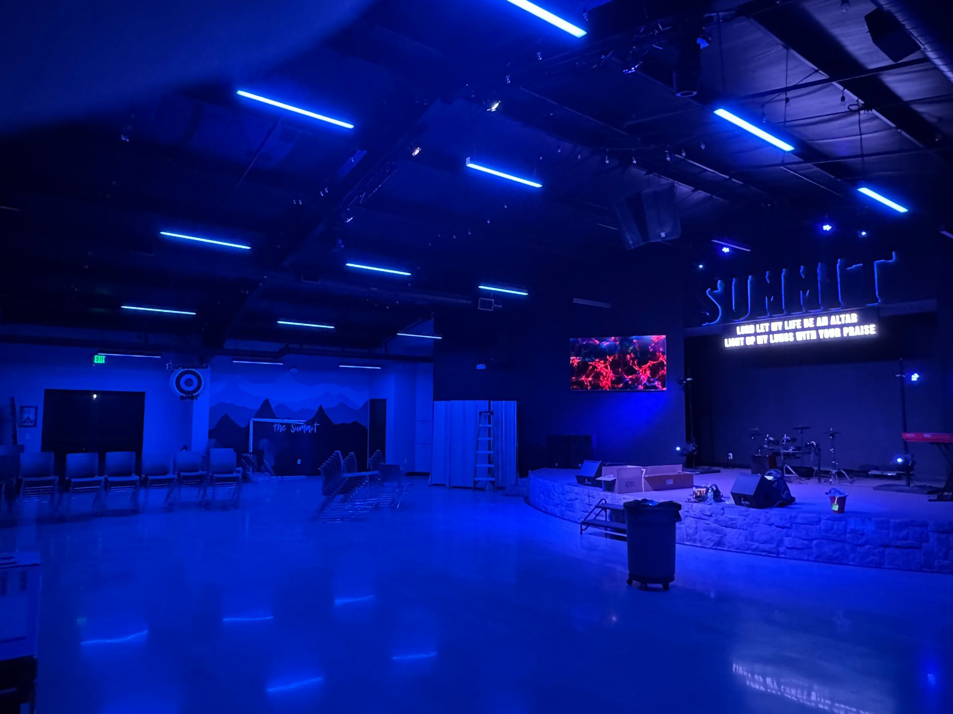 A large room with blue lights on the ceiling and a stage.