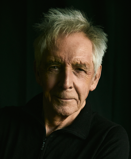 A man with gray hair is wearing a suit and tie and looking at the camera.