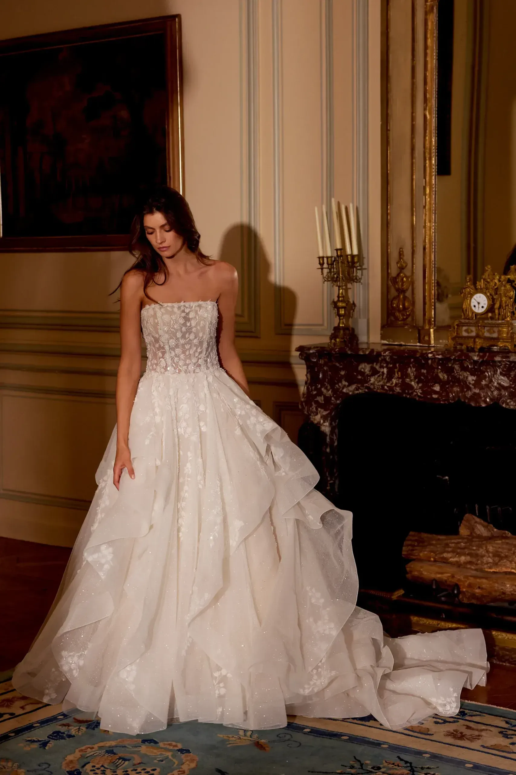 A woman in a wedding dress is standing in a room next to a fireplace.