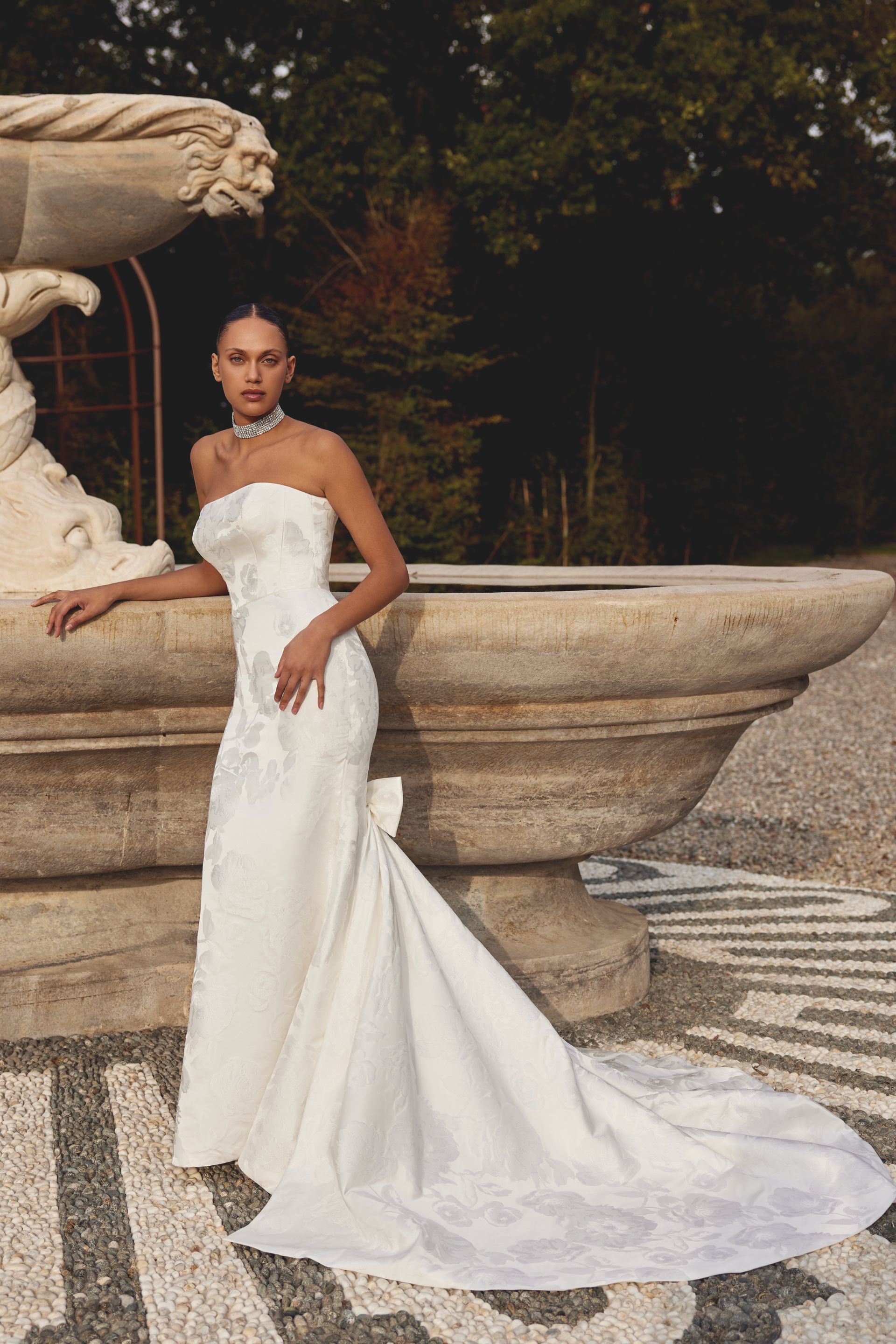 A woman in a white wedding dress is standing next to a fountain.