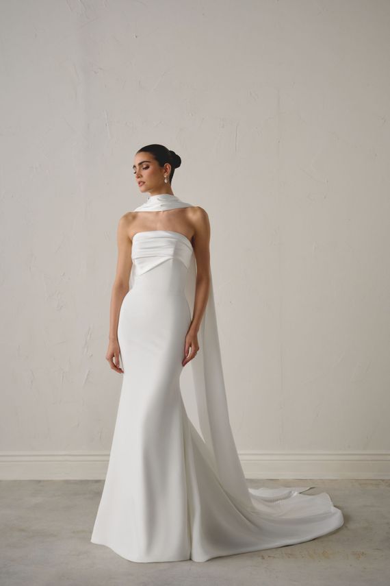 A woman in a white wedding dress is standing in front of a brick wall.