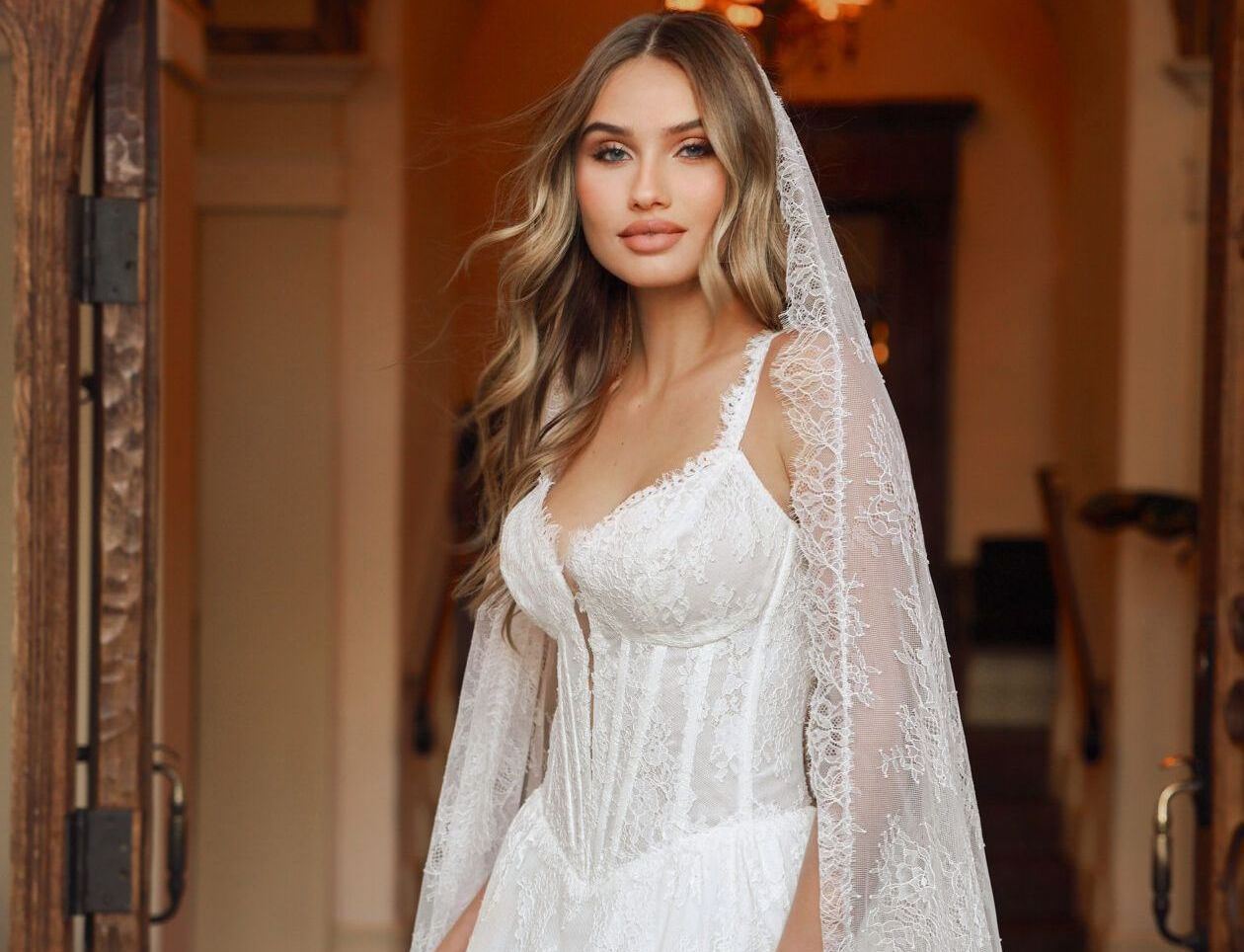 A woman in a wedding dress and veil is standing in front of a door.
