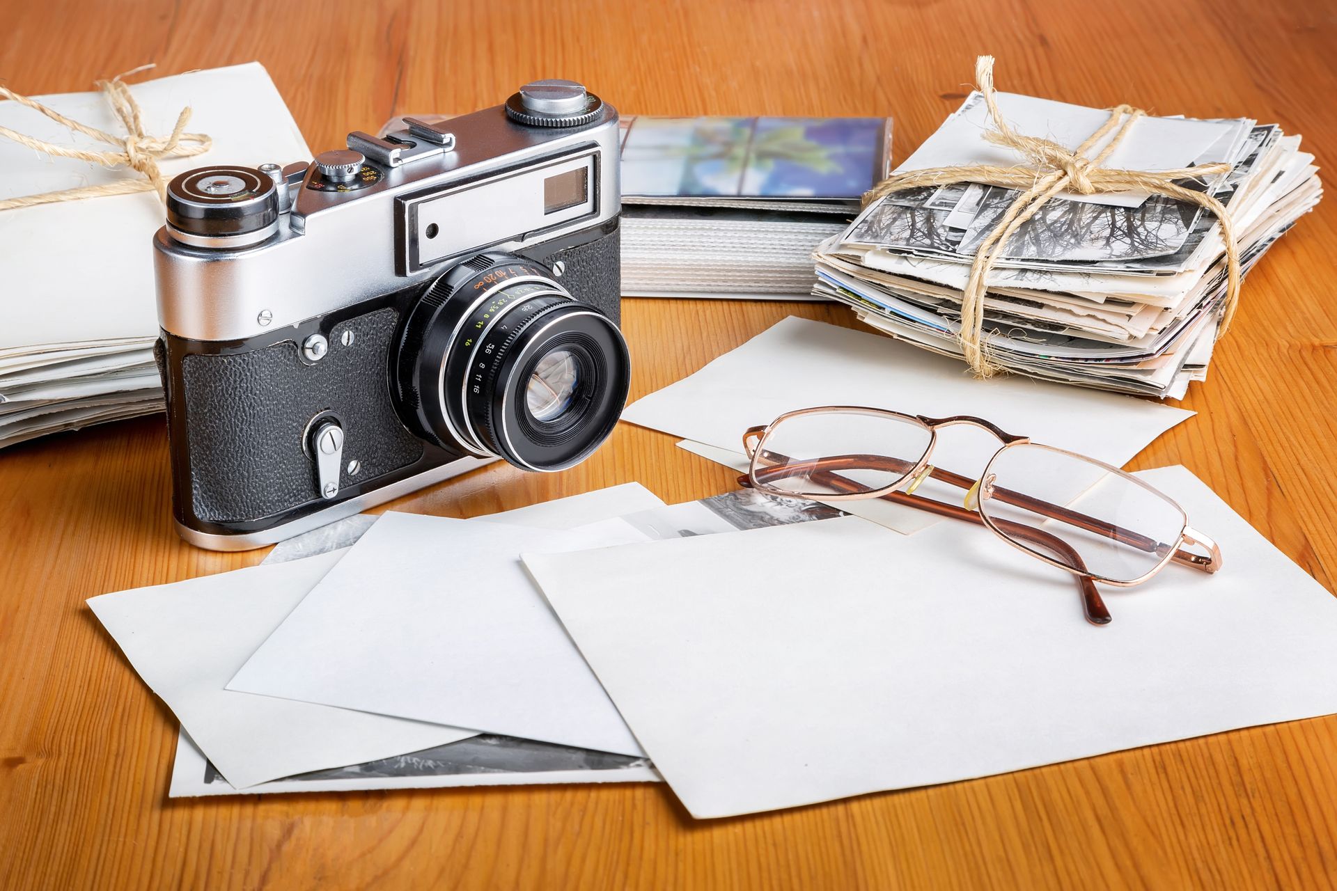 Vintage camera, postcards, eyeglasses, and a bundle of old cash on a wooden table.