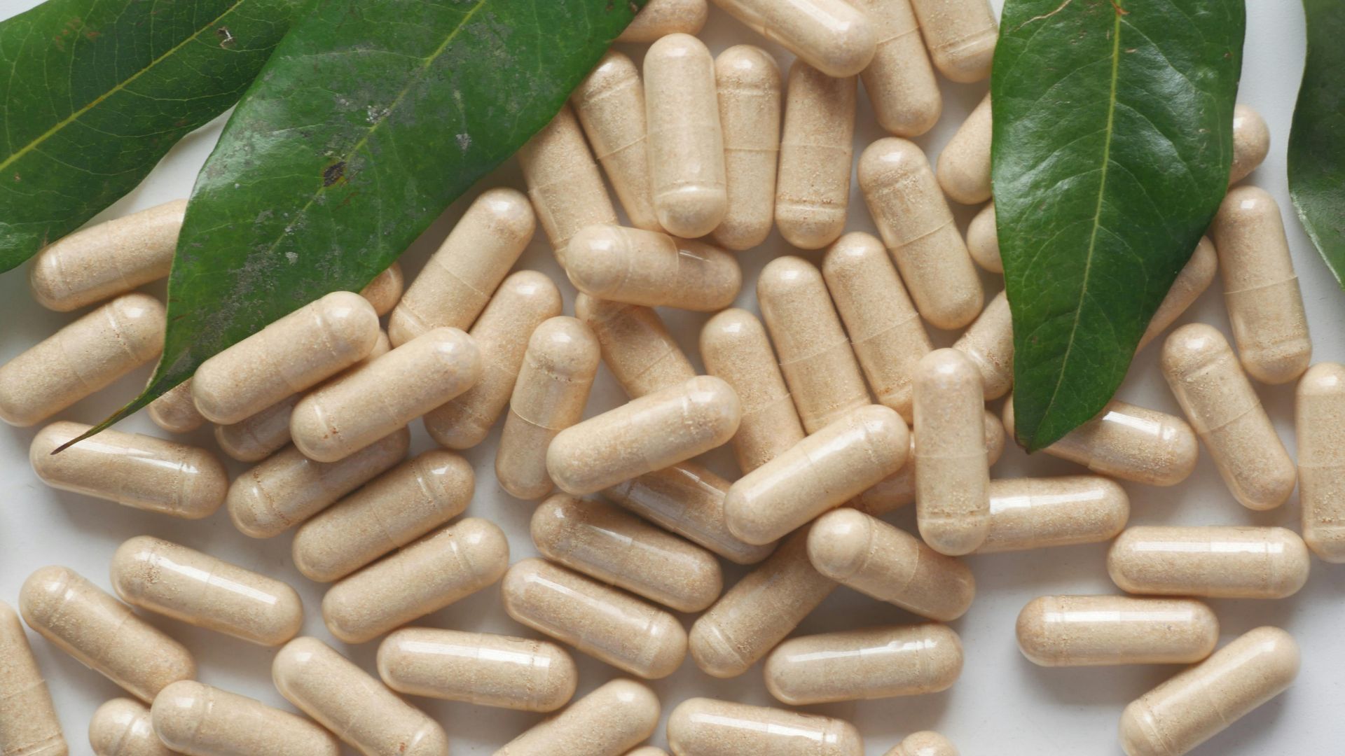 A pile of pills with green leaves on a white surface.