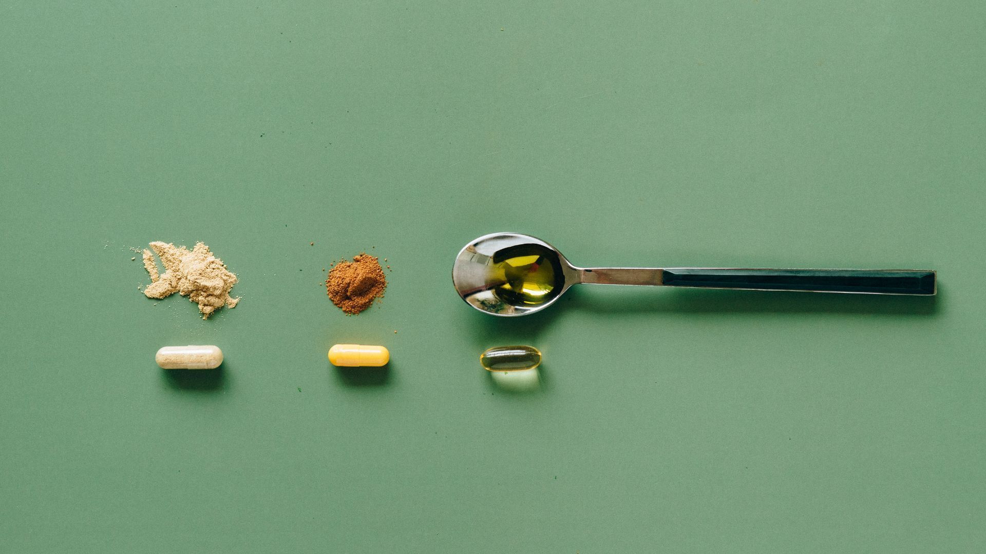 A spoon filled with oil and pills on a green surface.