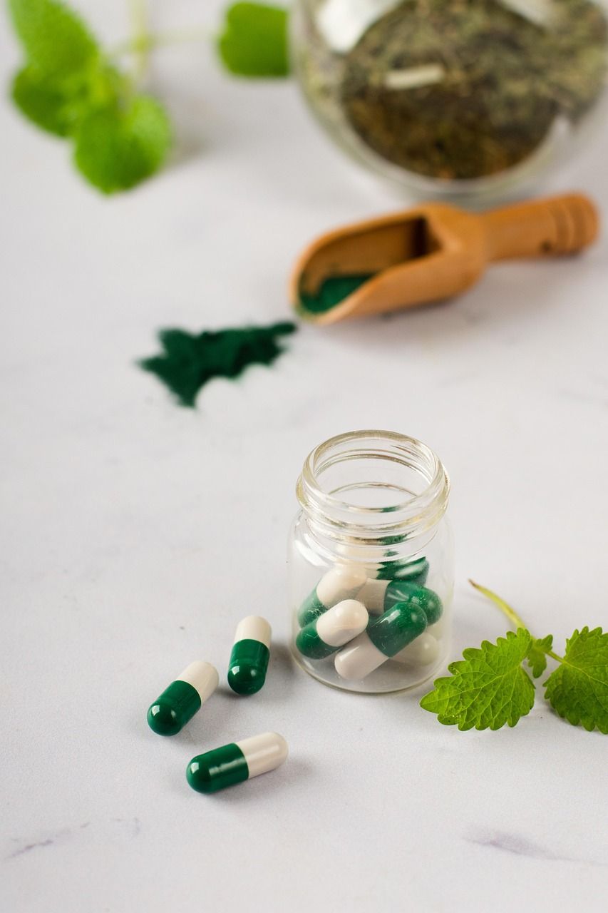 A glass jar filled with green and white capsules next to a wooden spoon.