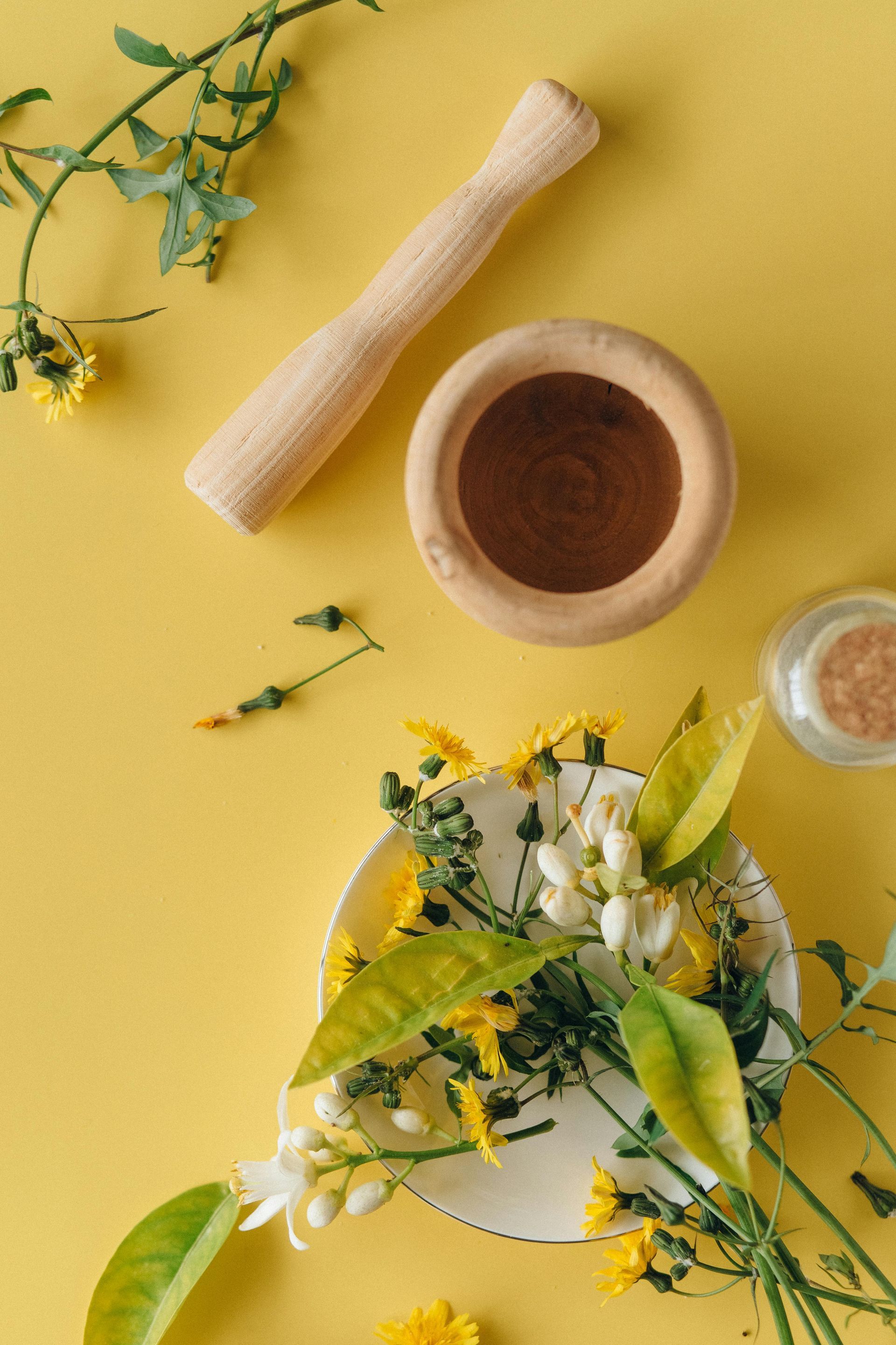 A mortar and pestle and a bowl of flowers on a yellow background.