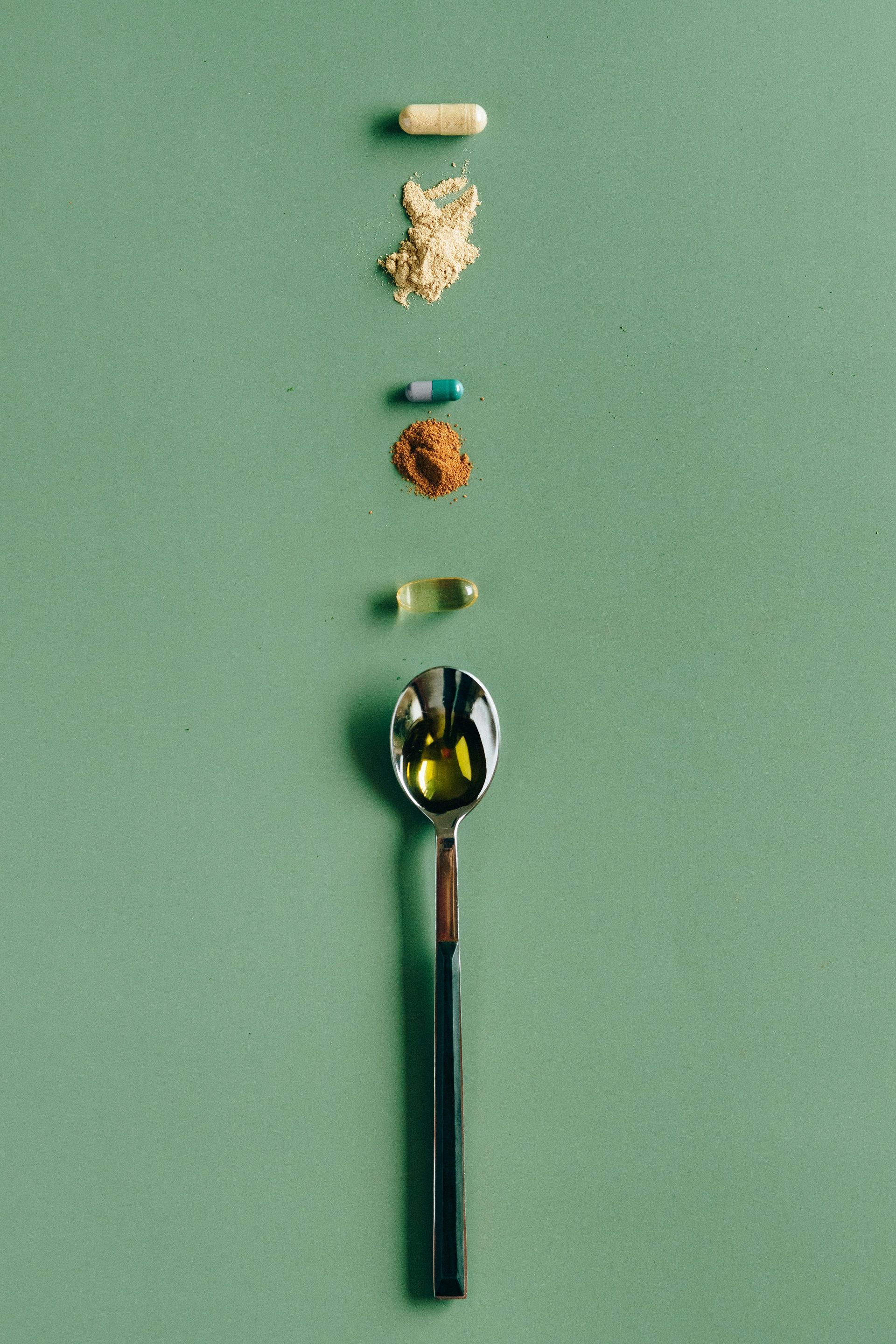 A spoon filled with different types of pills on a green background.