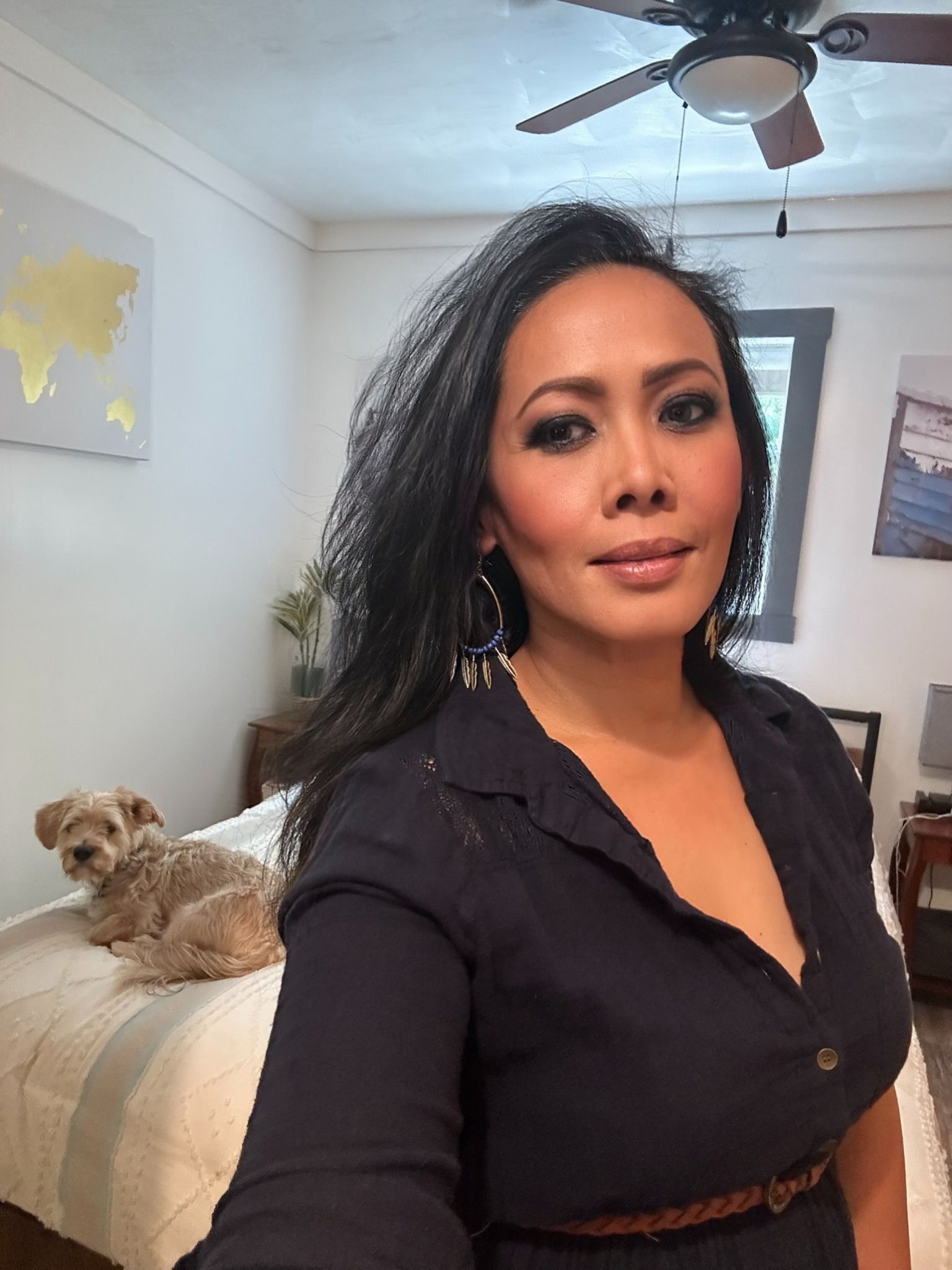 A picture of Tessa Tristianti in dark dress, looking at the camera, with a small dog on a bed in a room.