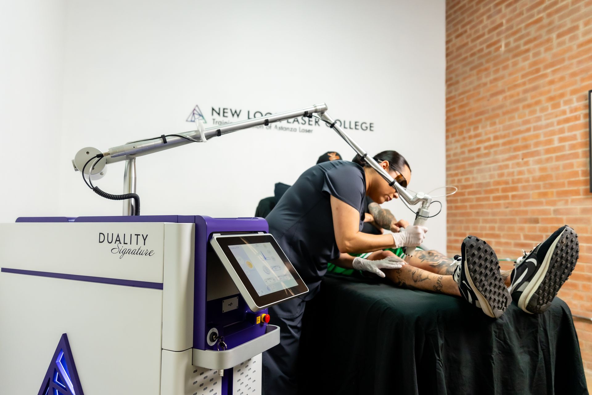 Person using laser tattoo removal device on a patient's leg in a clinic. Purple and white equipment.