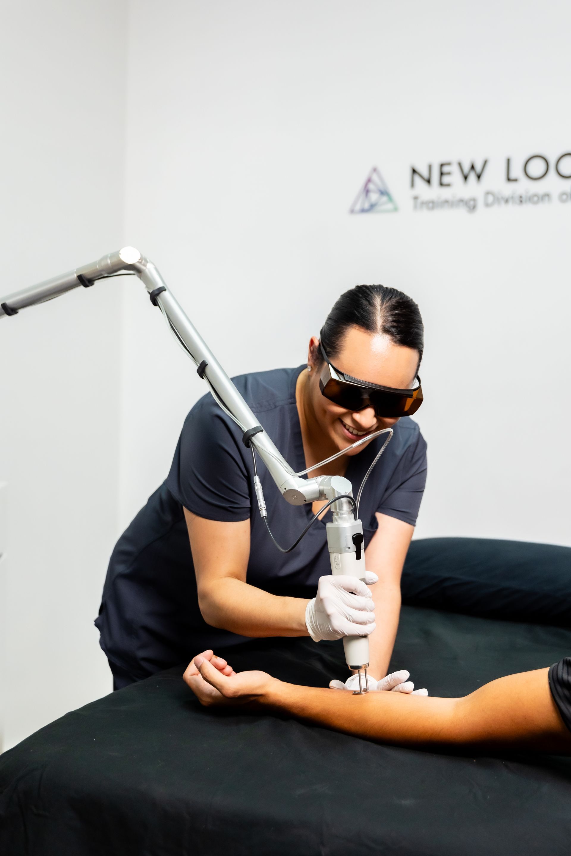 A person using a laser device on a patient's arm. Wearing protective eyewear in a medical setting.
