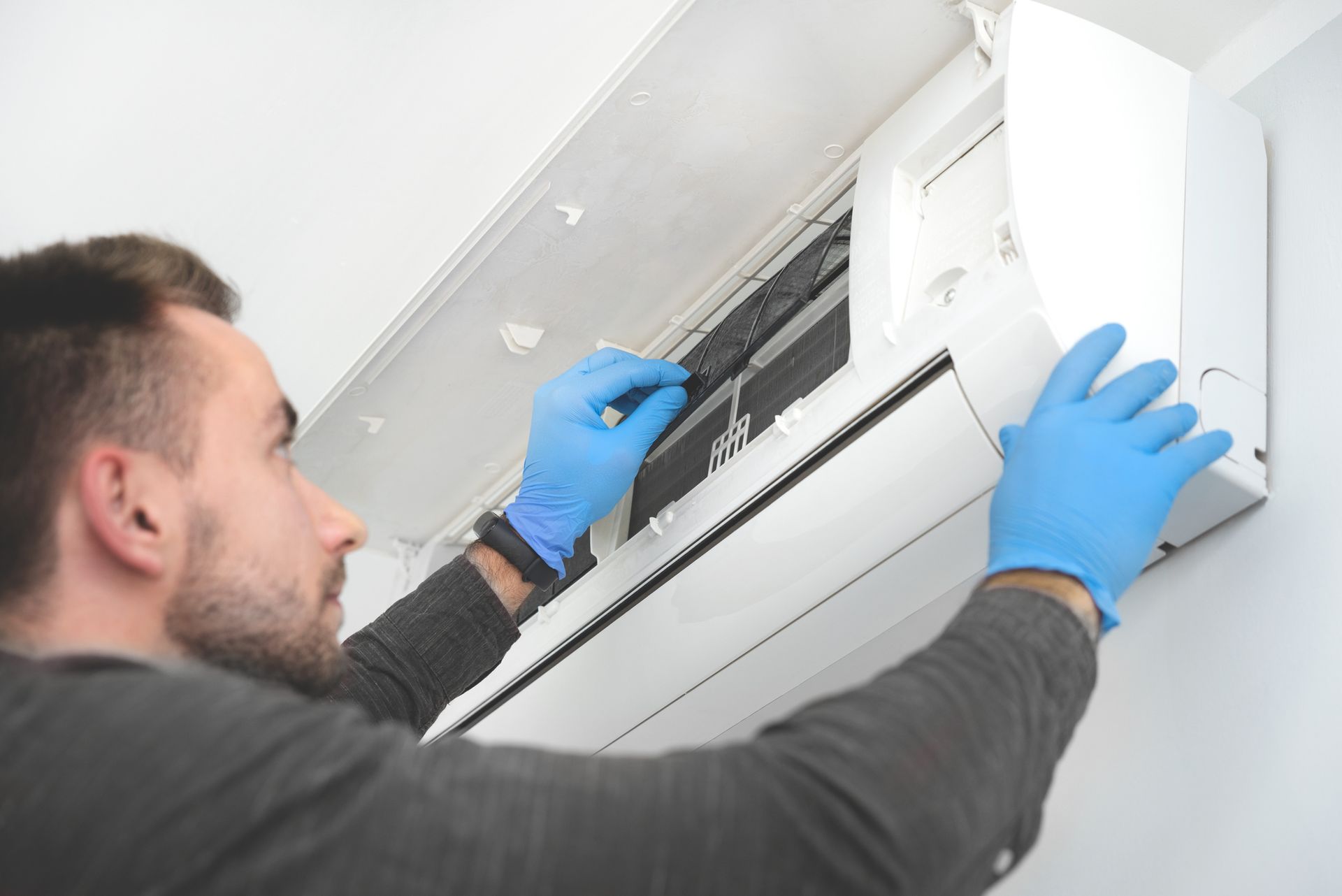 A man wearing blue gloves is cleaning an air conditioner.