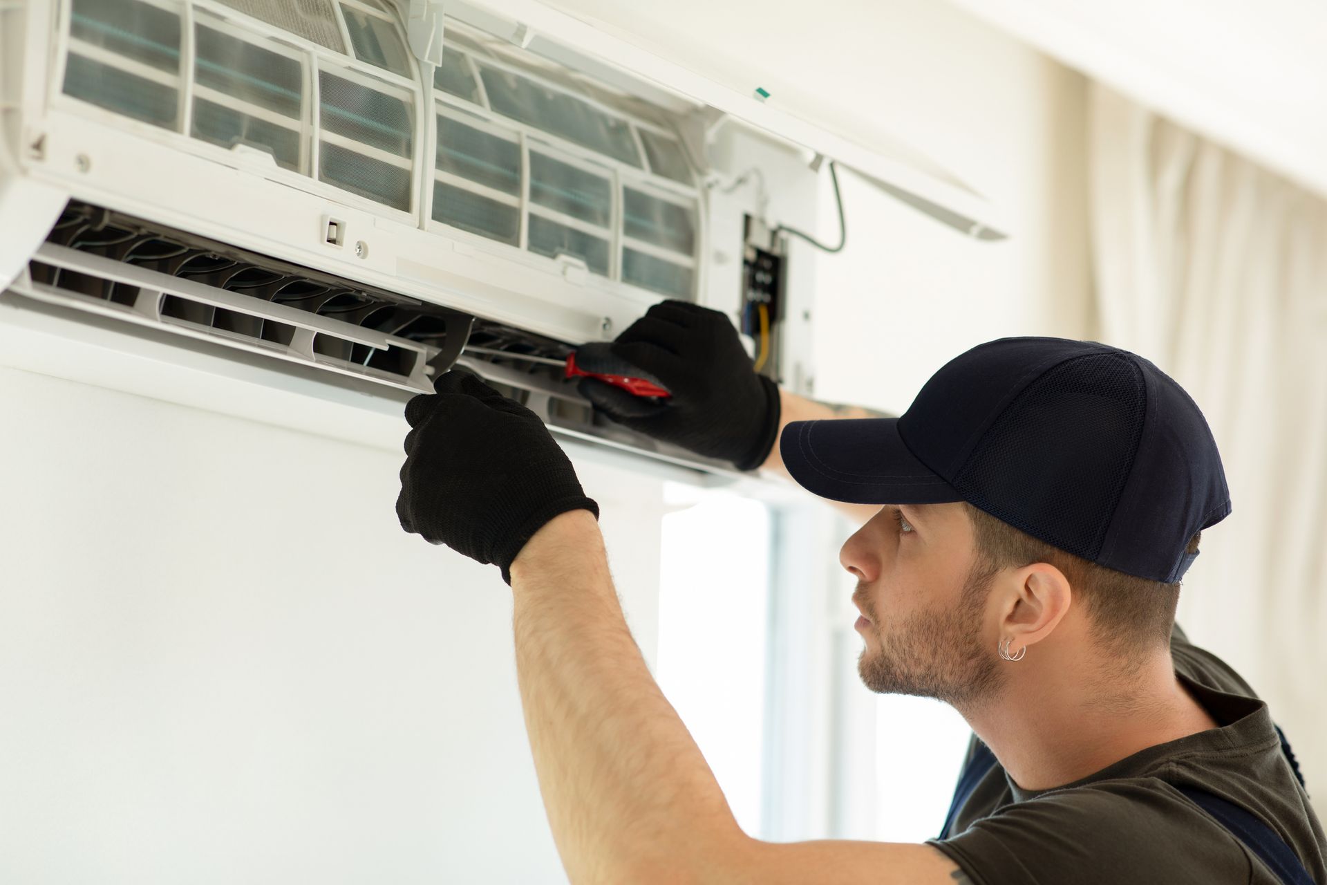 A Reliable Heating & Cooling technician is fixing an air conditioner with a screwdriver.