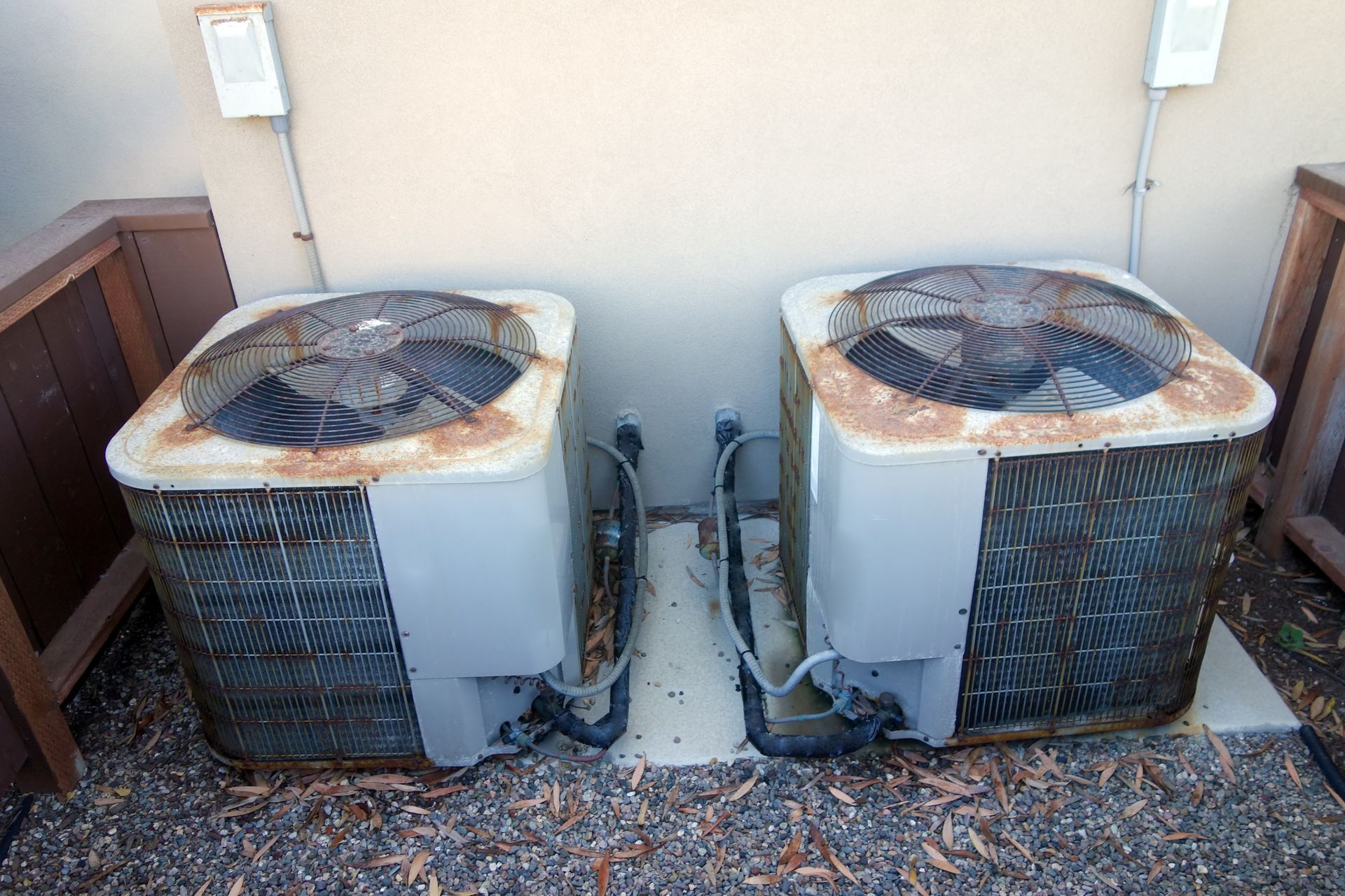 Two rusty air conditioners are sitting next to each other on the side of a building.