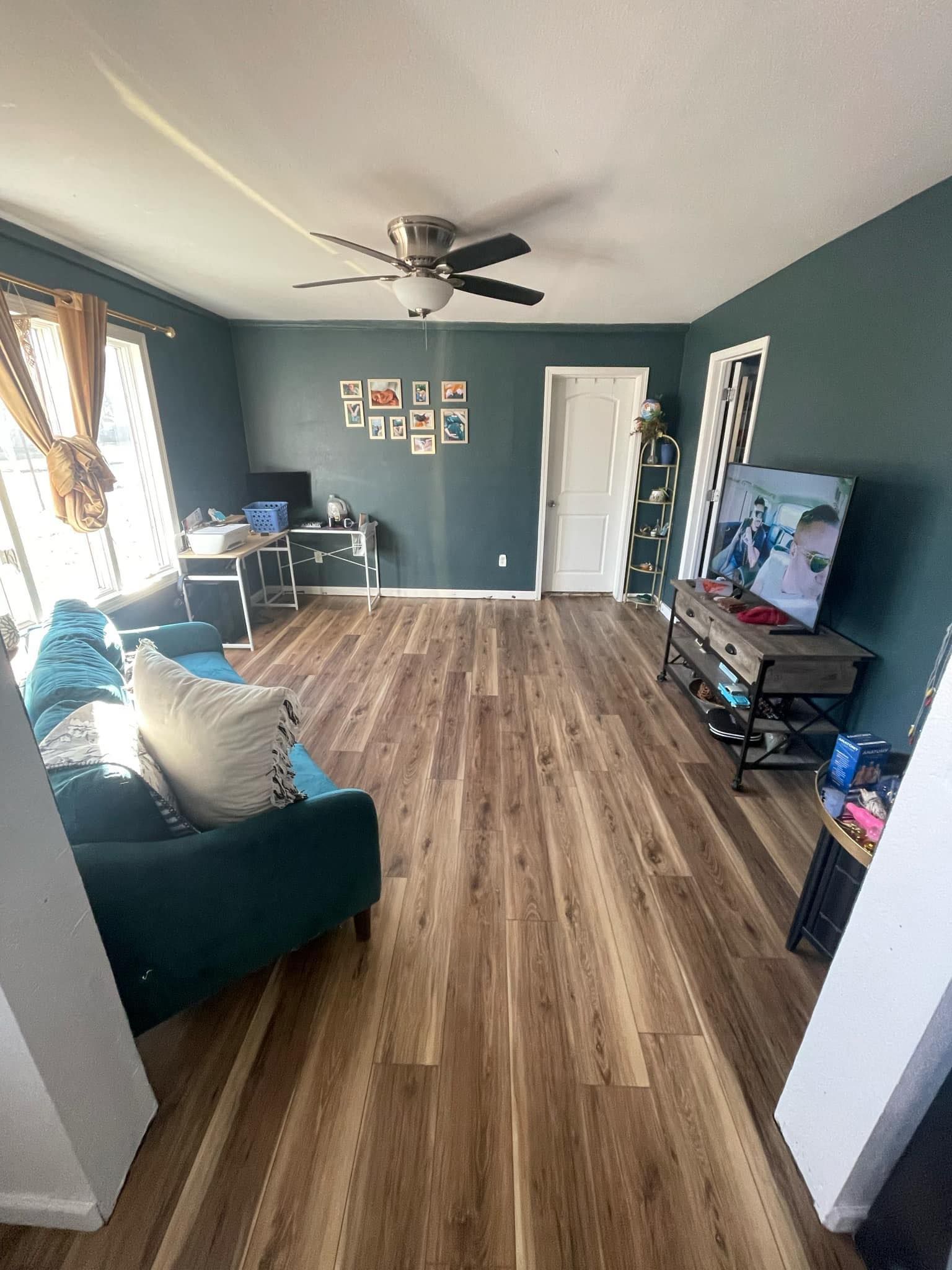 Living room with teal walls, wood floors, teal sofa, and TV.