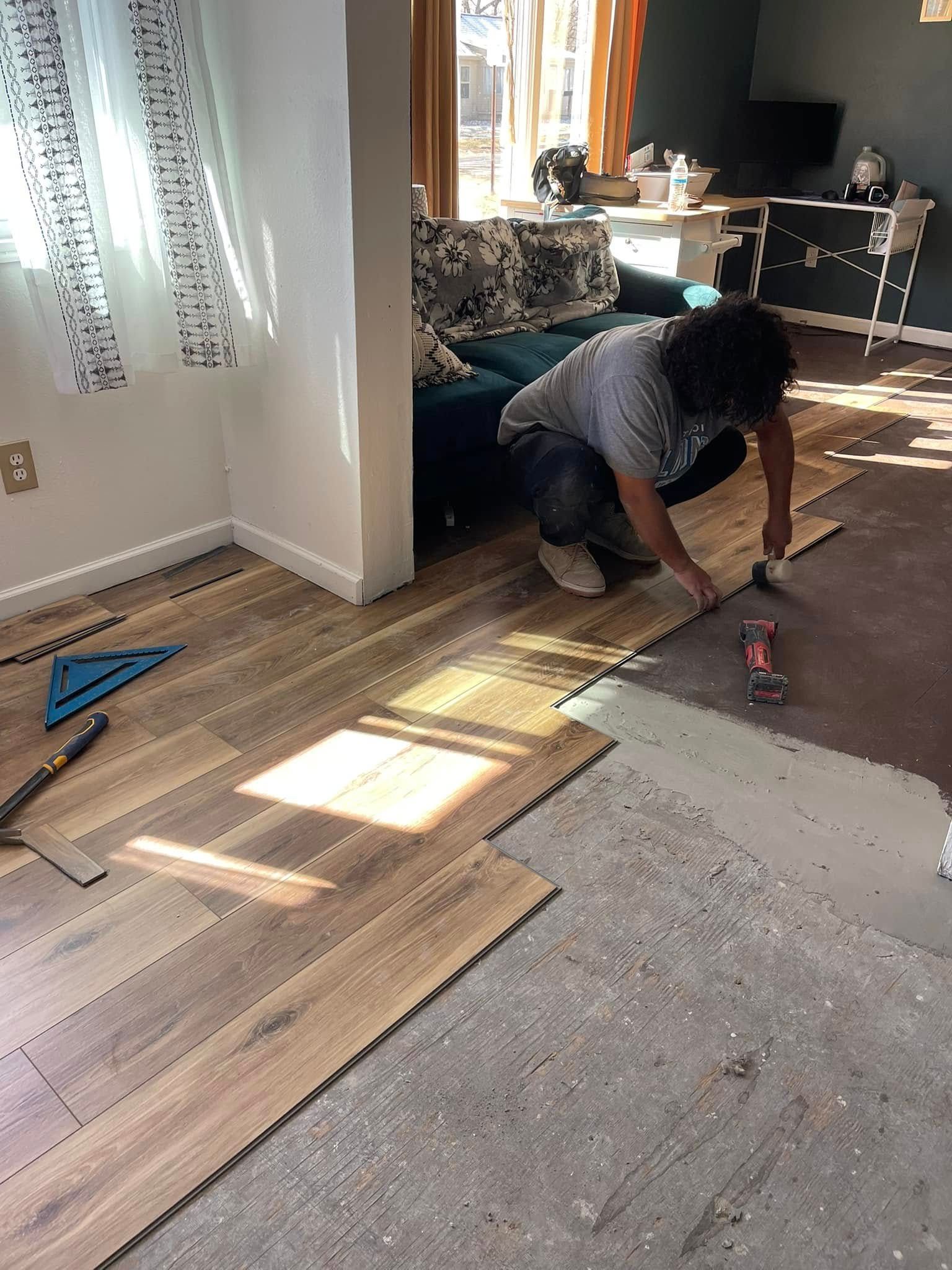 Person installing wood-look flooring in a room. Sunlight streams in.