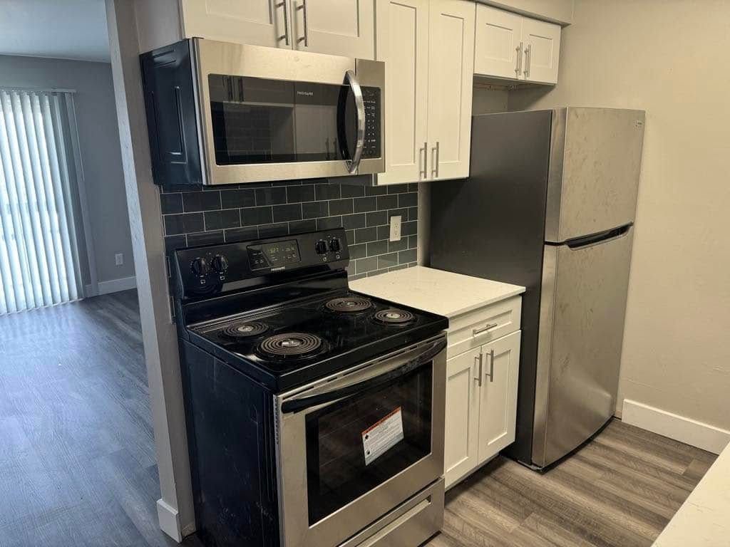 Kitchen with stainless steel appliances: oven, microwave, and refrigerator, white cabinets, gray tile backsplash.