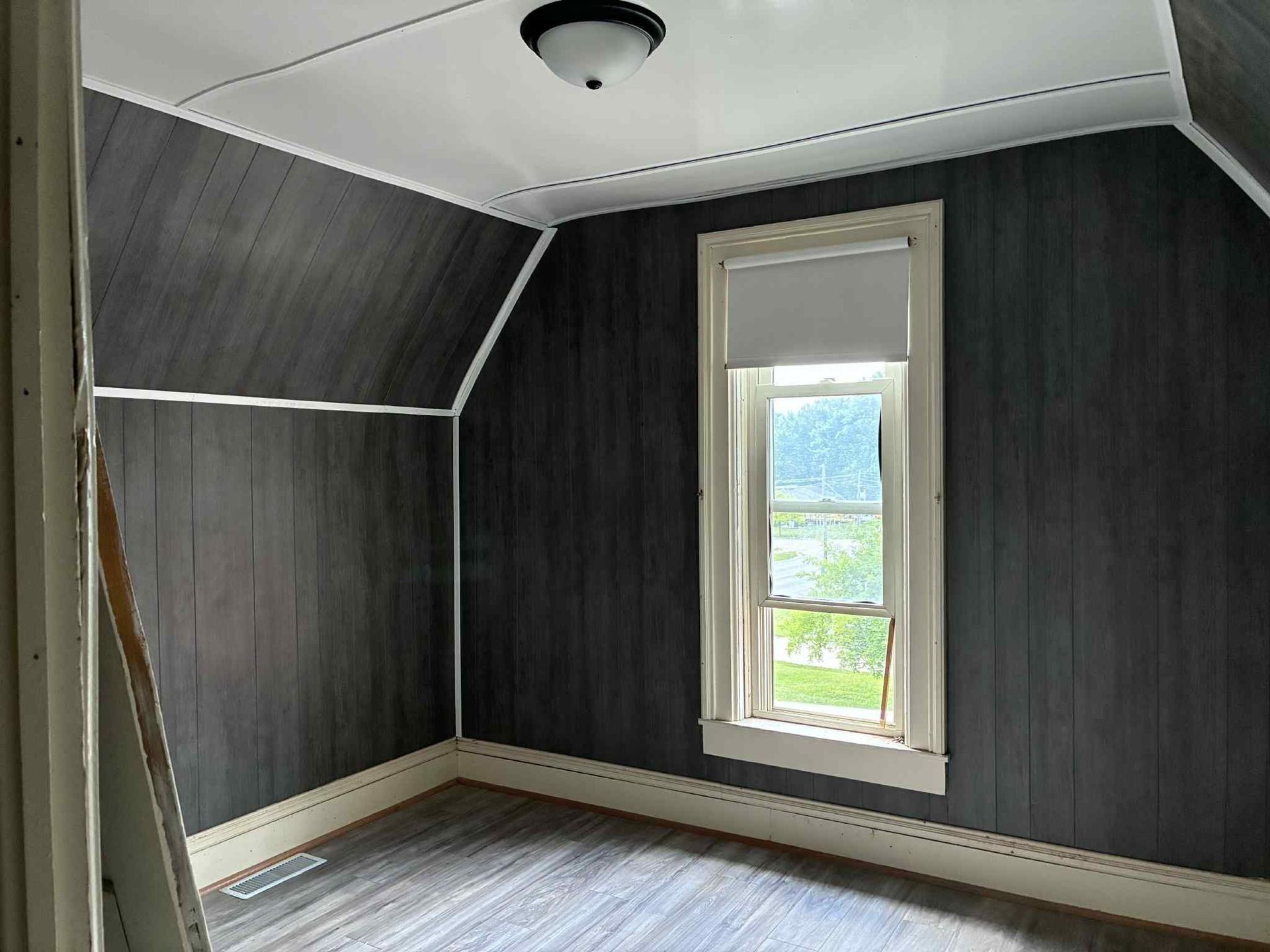 Empty room with dark grey paneled walls, white ceiling, and a window with a light colored shade.