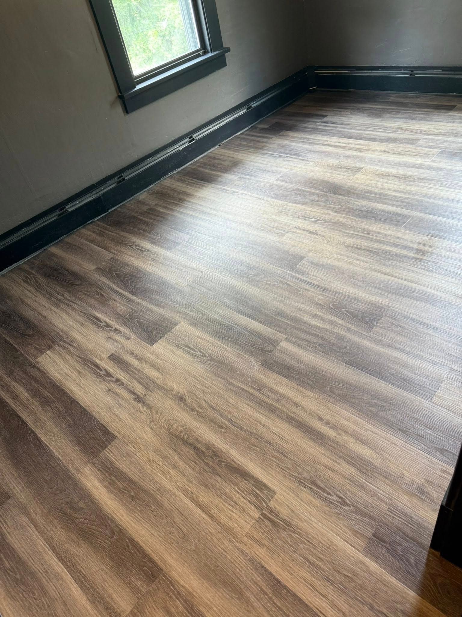 Dark wood-look flooring in a room with a window and dark trim.