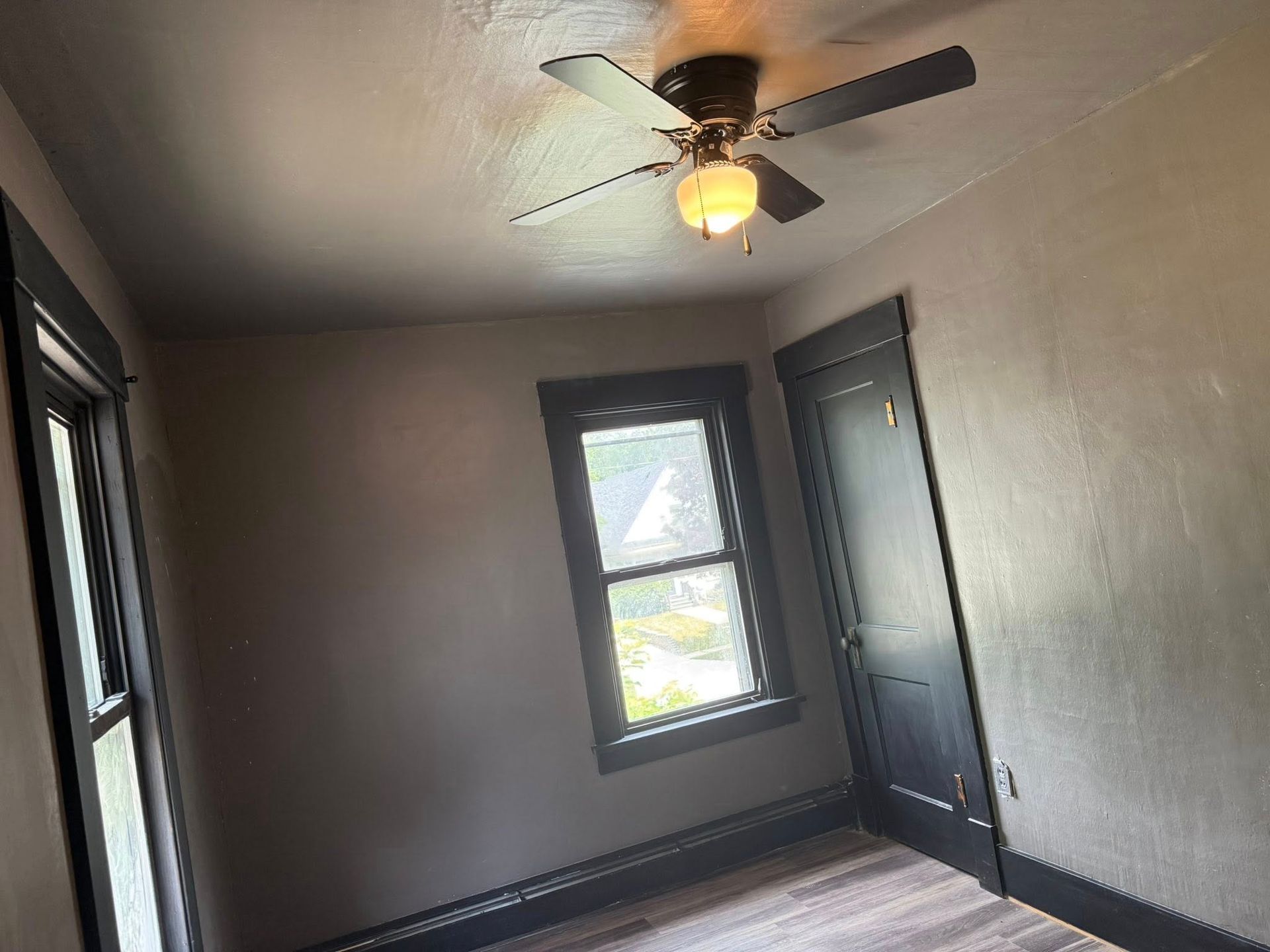 Empty room with dark trim, walls, and a ceiling fan. Window and door.