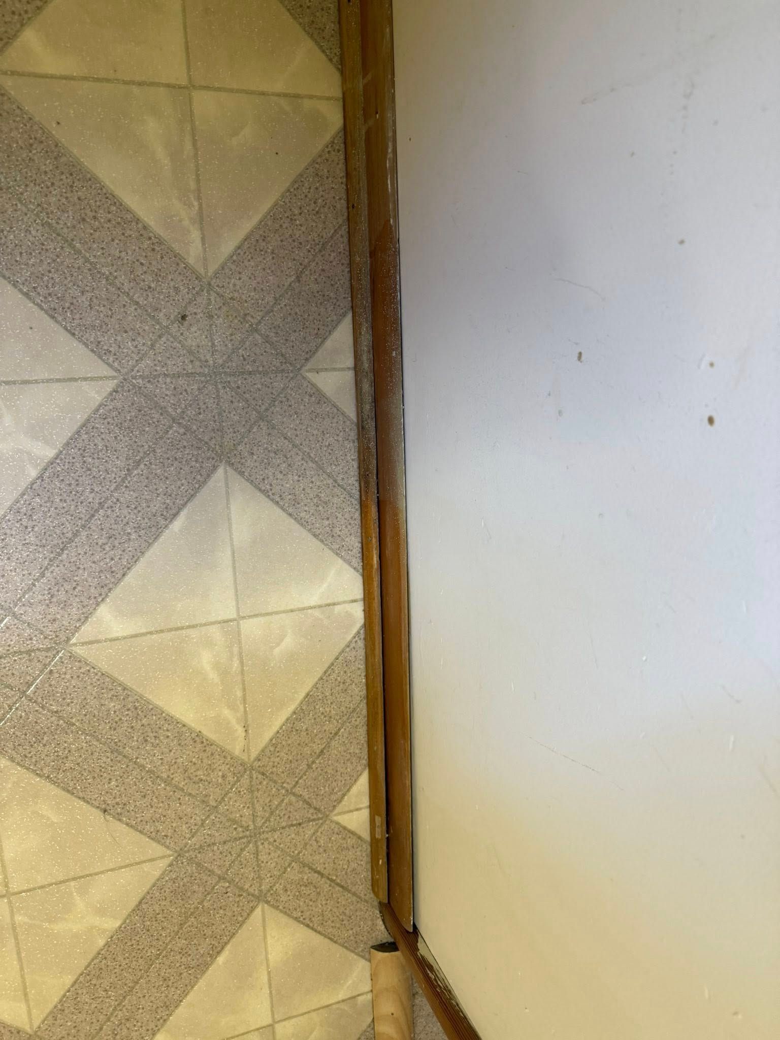 Brown wooden trim next to a white wall and patterned beige and gray tile floor.