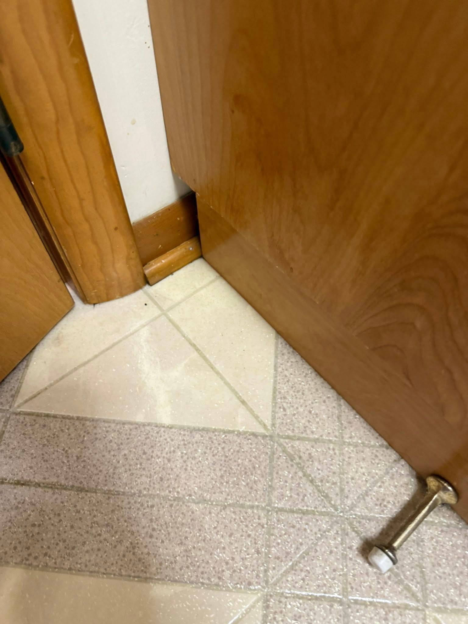 A partially opened wooden door with a doorstop on a tiled floor.