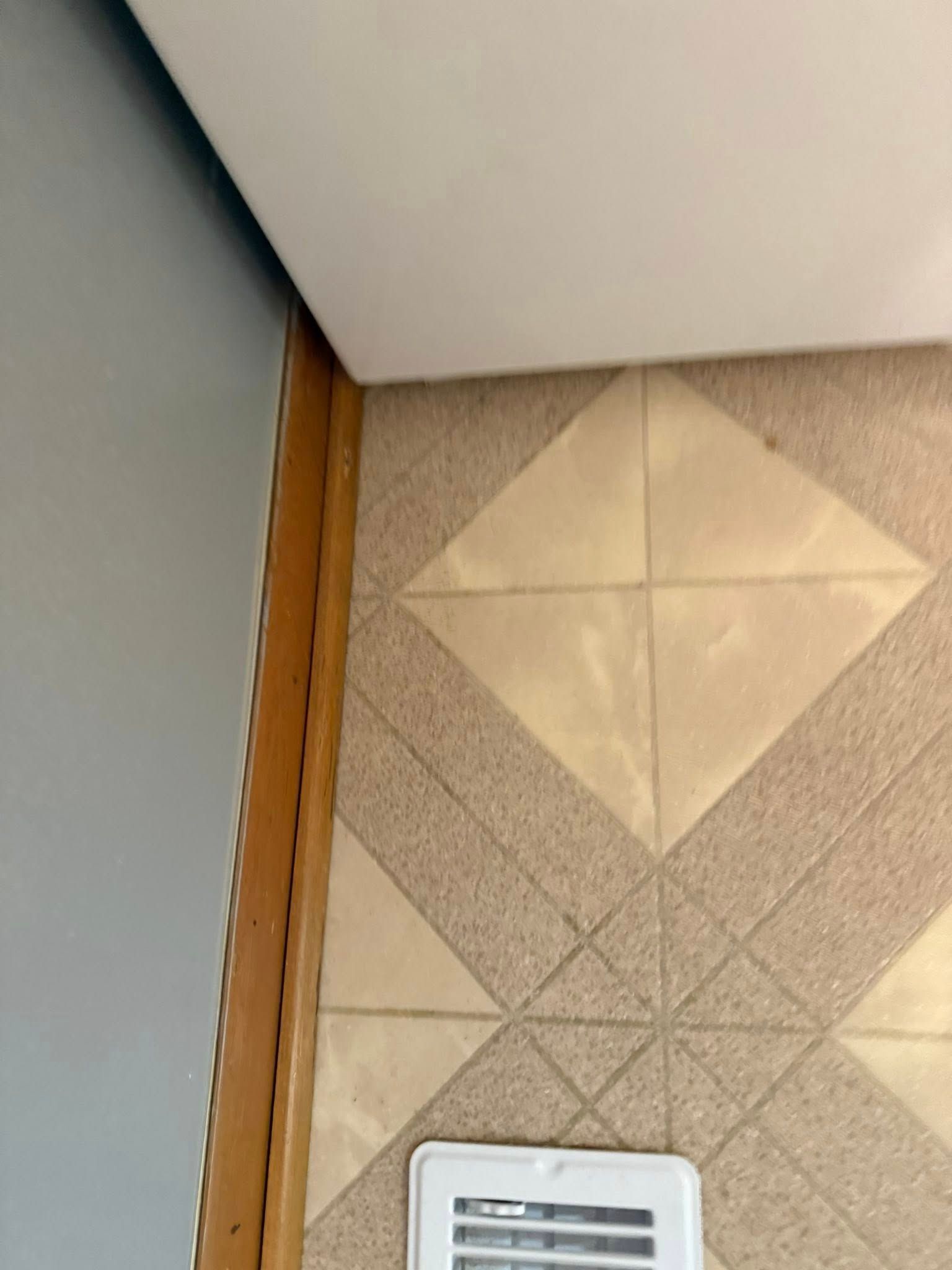 Corner of a room with tan tile pattern, white ceiling, gray wall, and wood trim.