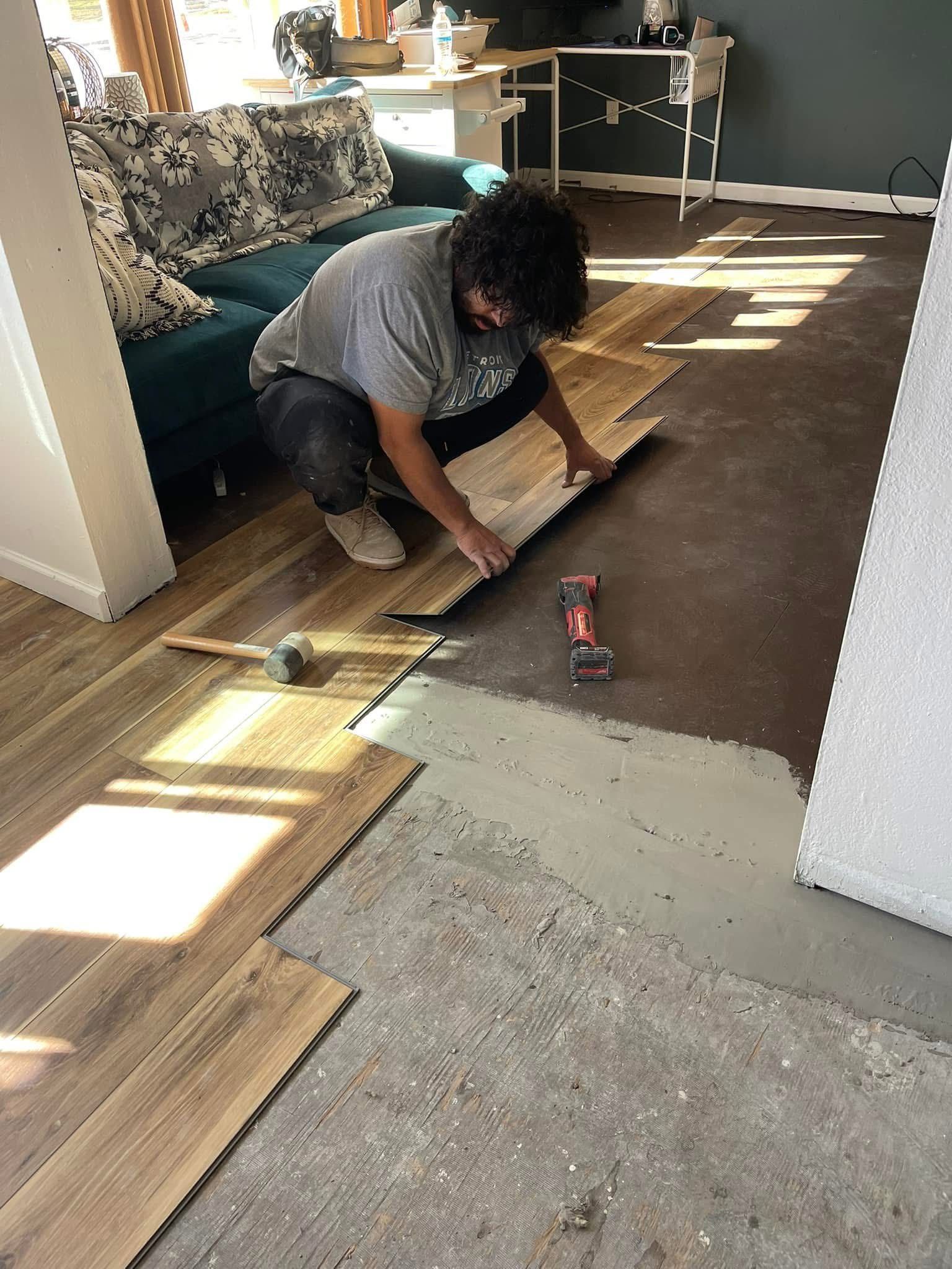 Person installing wood-look flooring on a concrete surface, crouching with tools in a home interior.