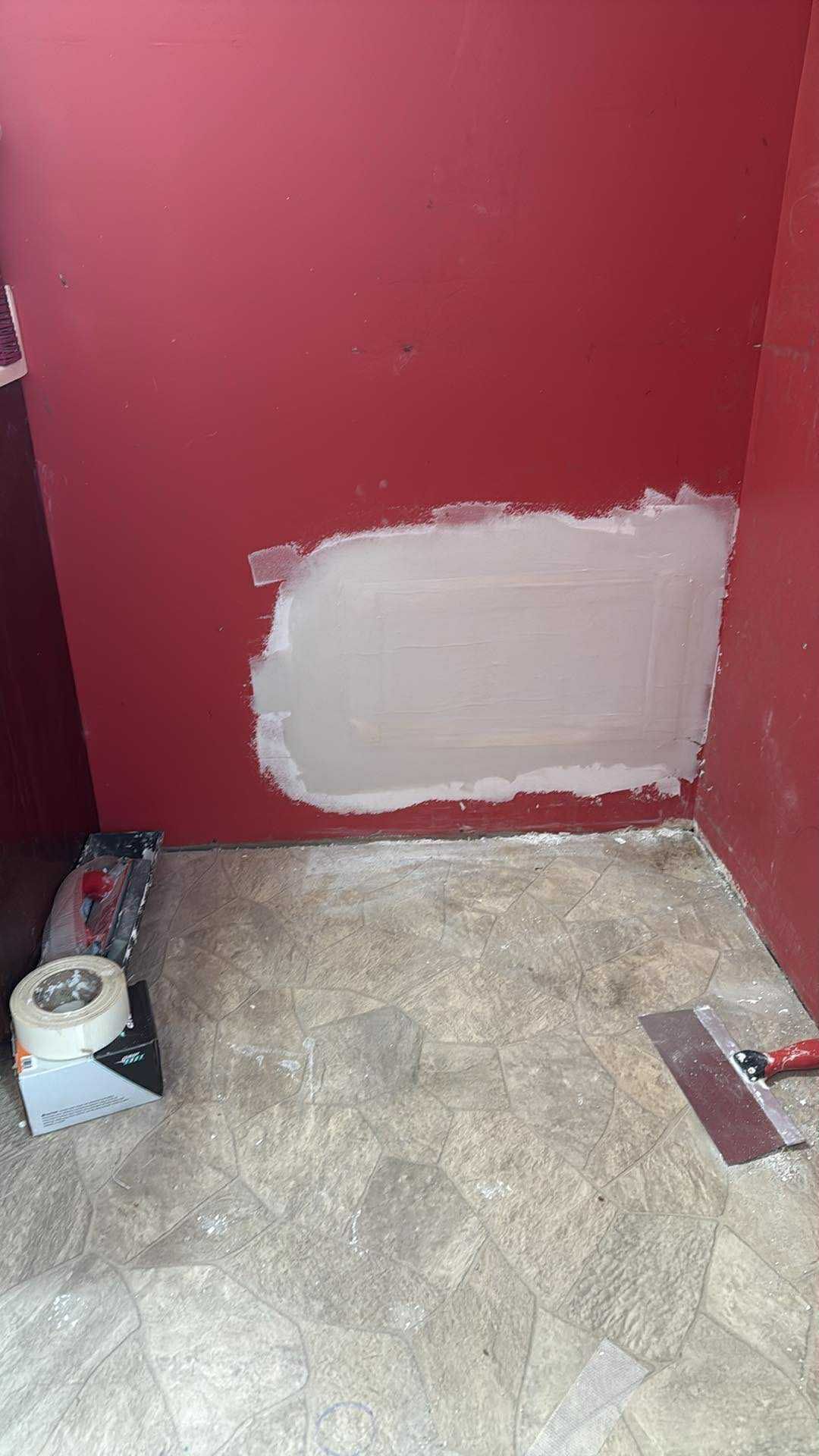 Red wall with a rectangular patch of compound; tools on floor.