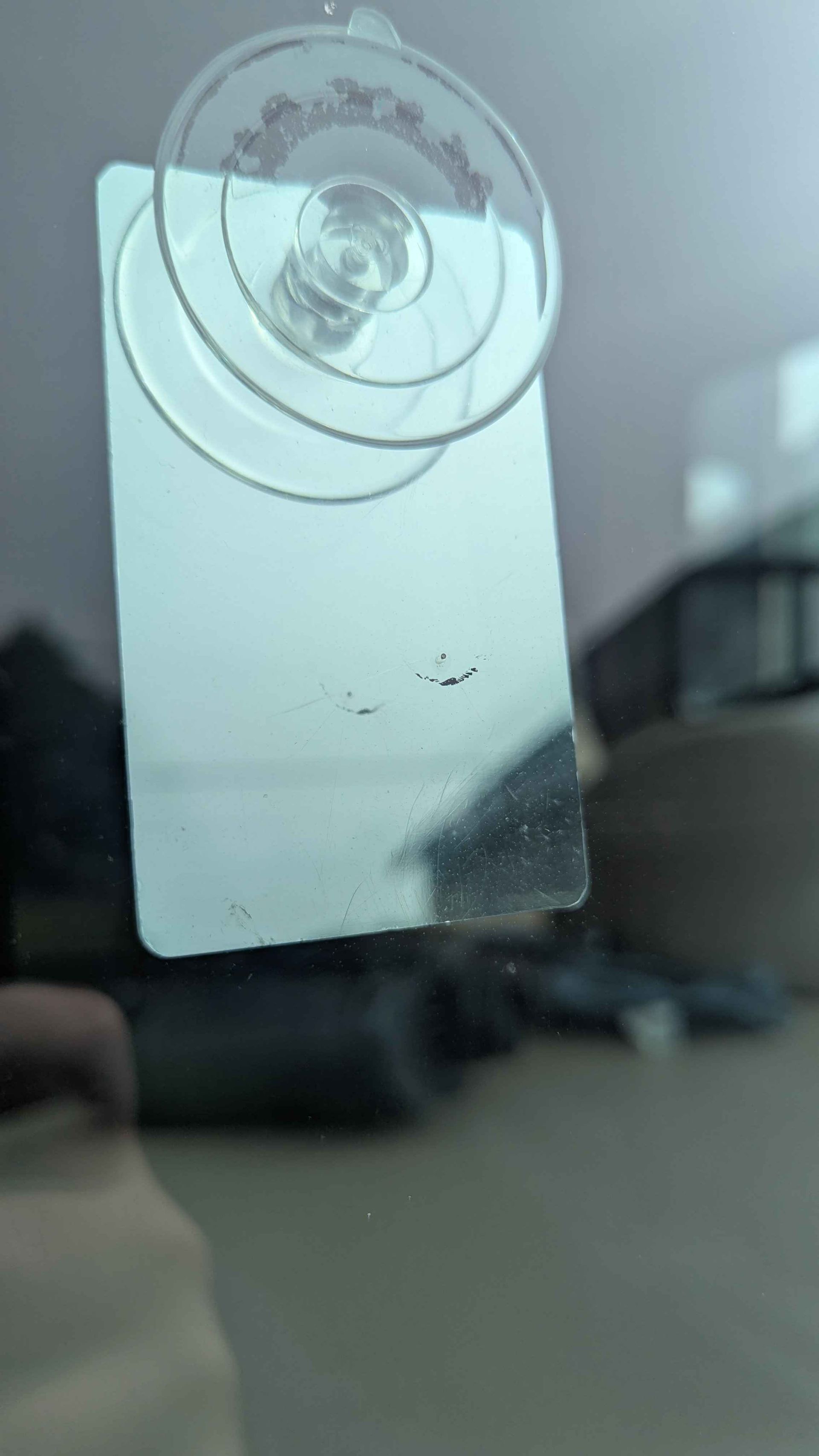 A small rectangular mirror with a suction cup attached, reflecting a blurry background.