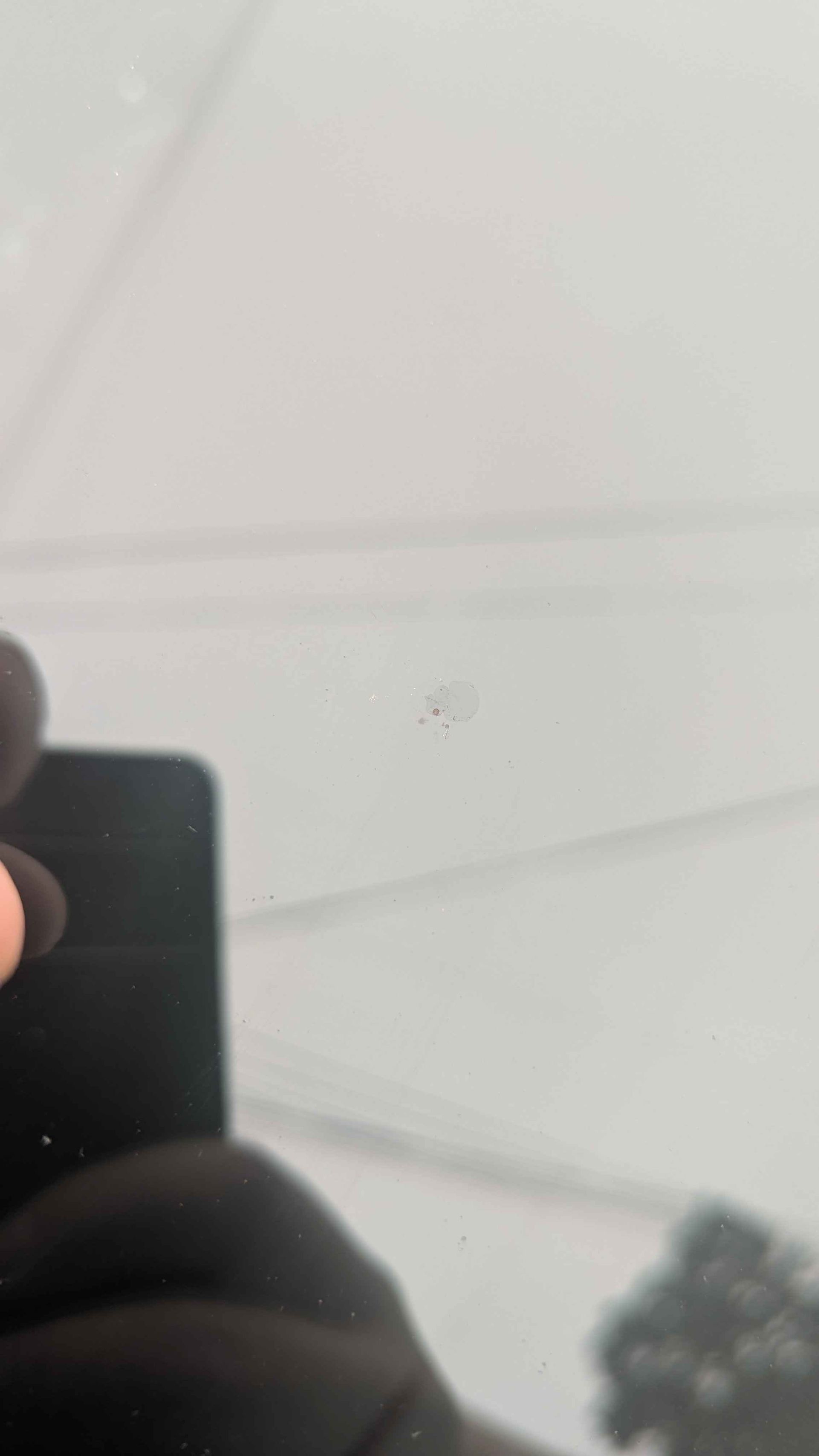 Close-up of a light-colored surface with a small, dark mark. A blurry reflection is visible below.