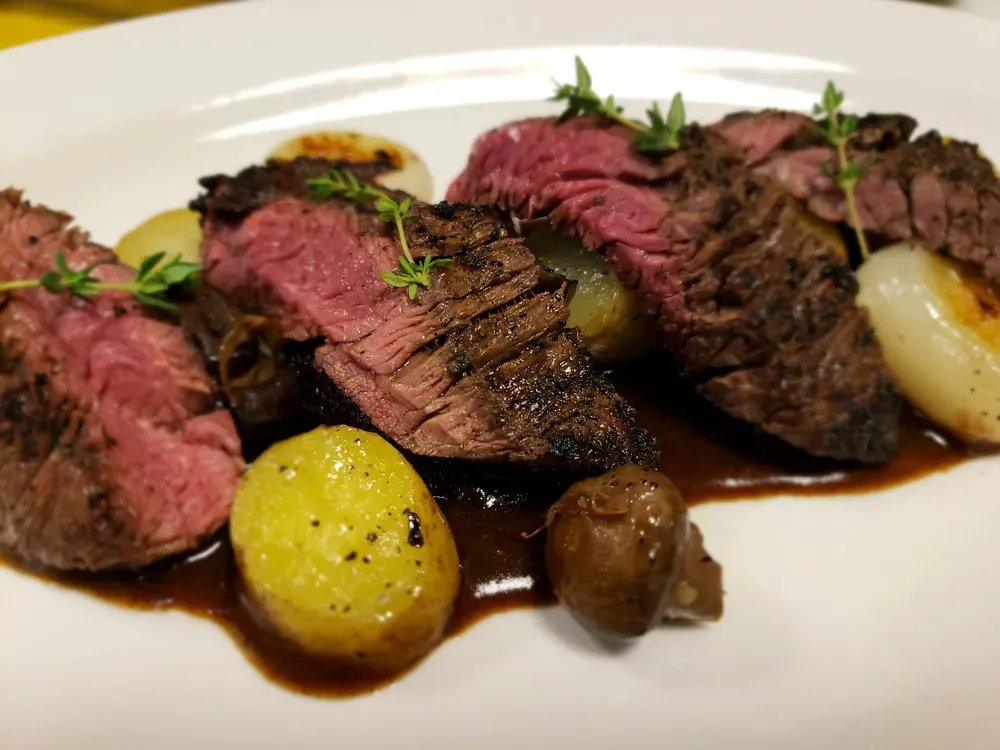Sliced steak with potatoes, mushrooms, and onions, drizzled with sauce and thyme garnish.