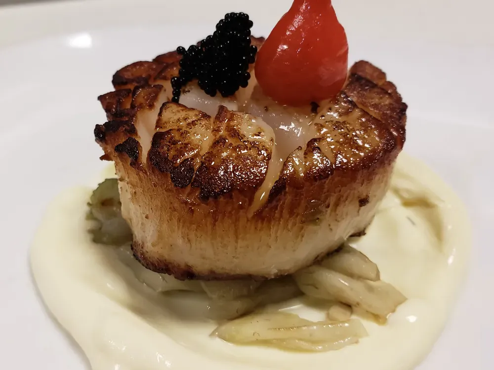 Seared scallop on a bed of artichoke, with a creamy sauce, caviar, and a red pepper garnish.