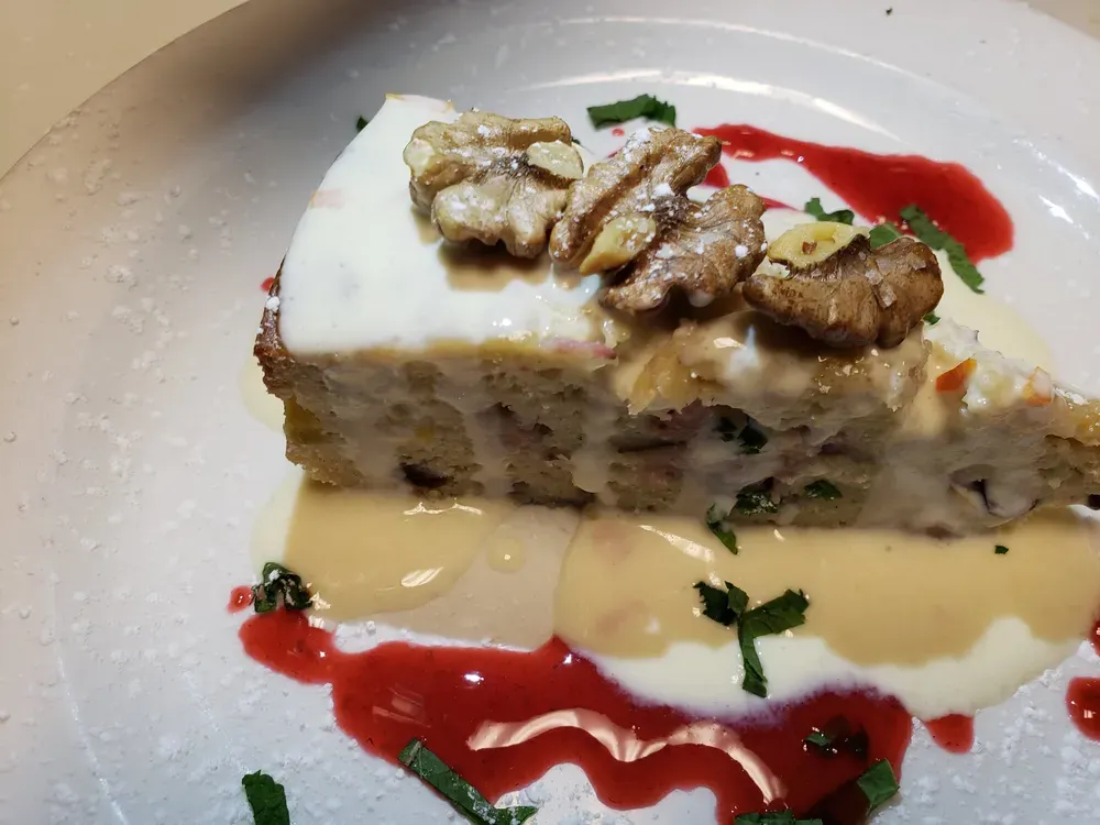 Slice of cake with cream frosting, walnuts, and sauces on a white plate.