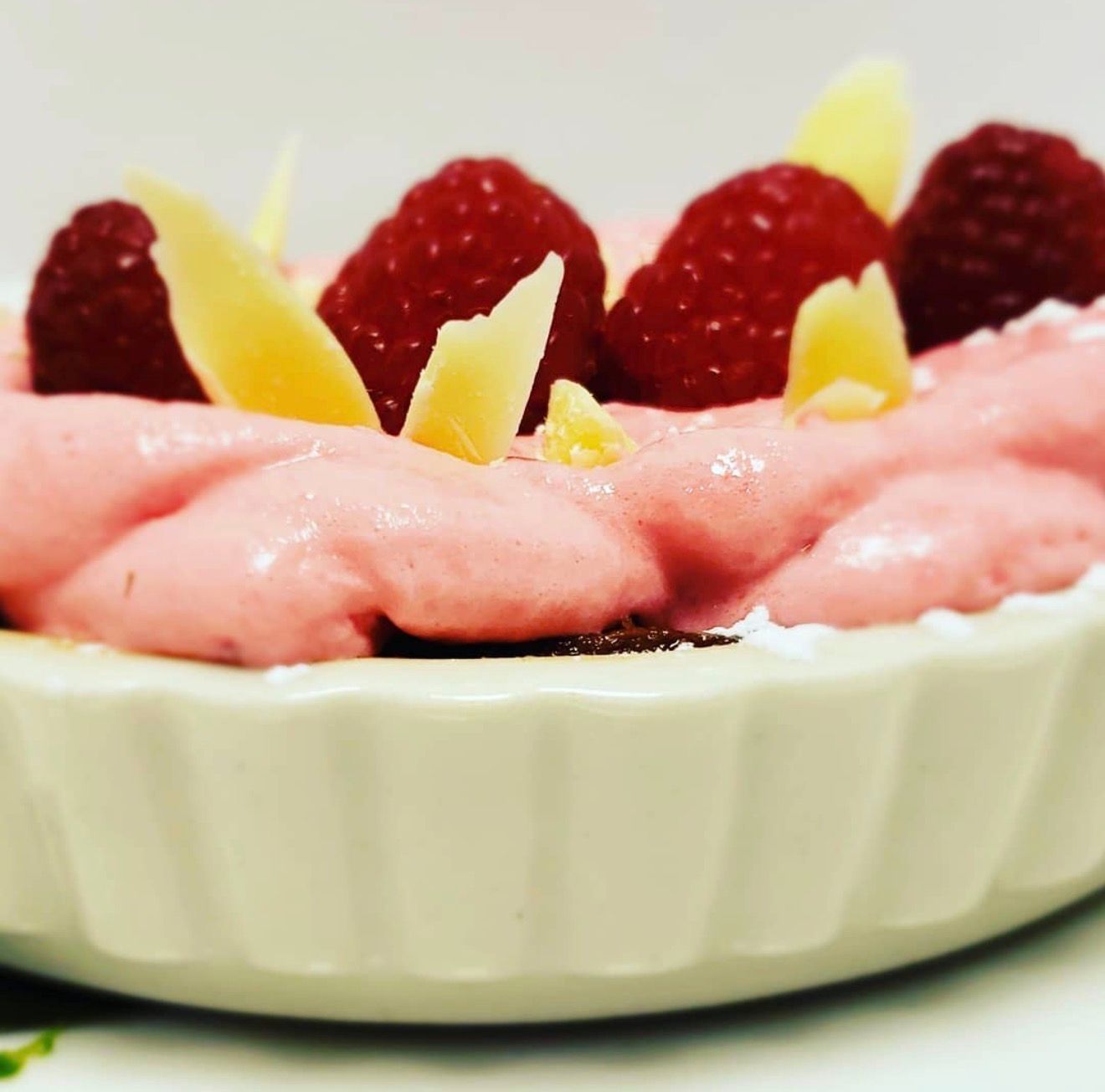 Raspberry dessert in white dish, pink cream topping, raspberries, white chocolate shavings.