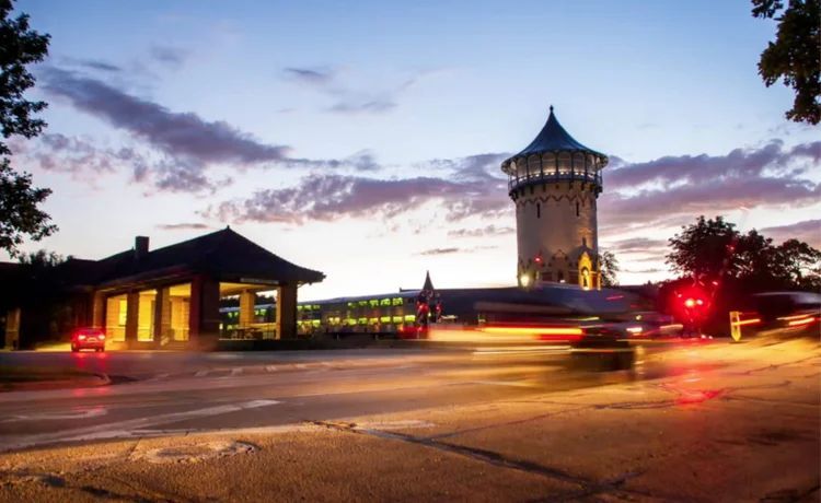 Tower and buildings at dusk, with blurred car lights on road.
