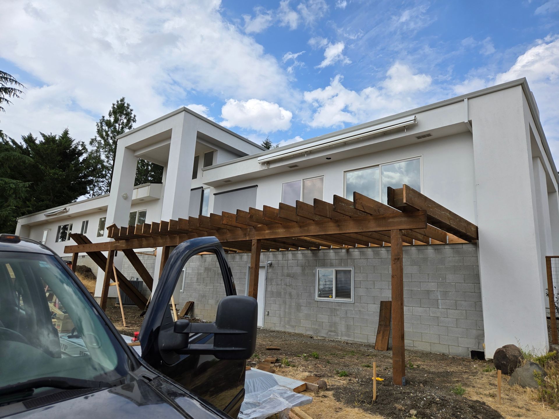 Modern white building with wood pergola; construction site with a truck in foreground.