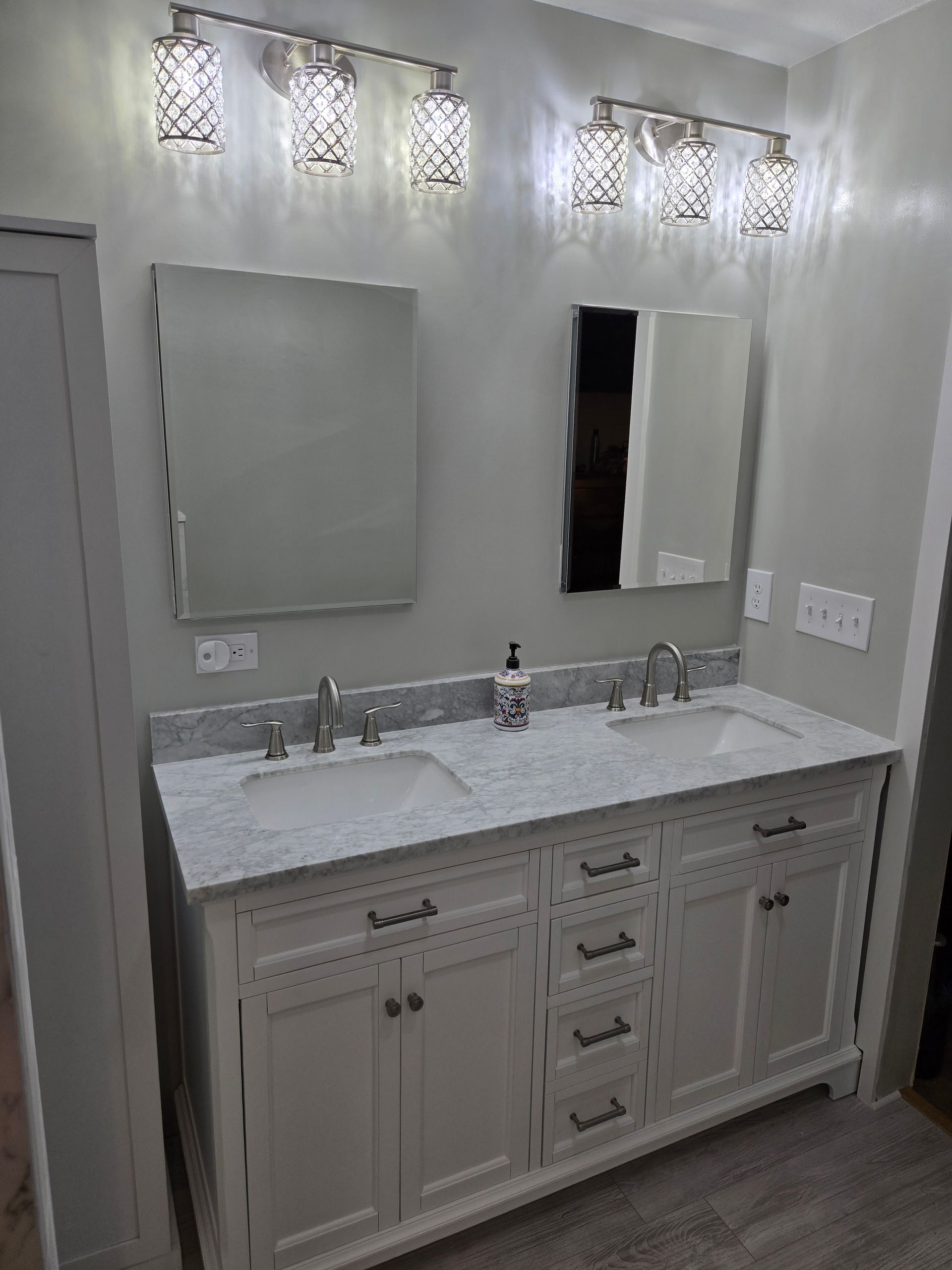 Bathroom with double vanity, white cabinets, granite countertop, two mirrors, and overhead lighting.