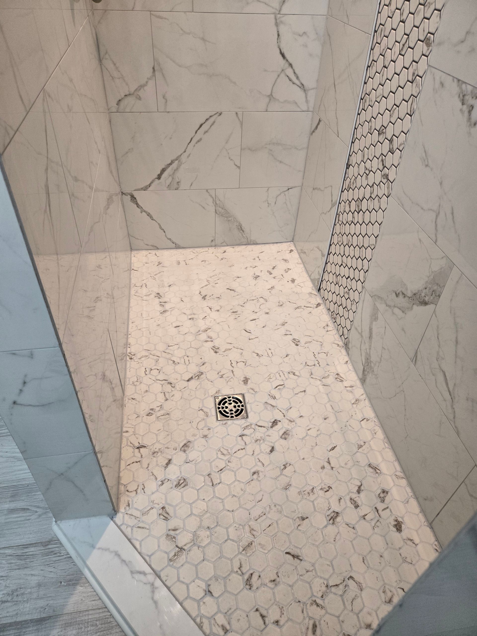 Shower with white marble walls and a mosaic tile floor, angled shape.