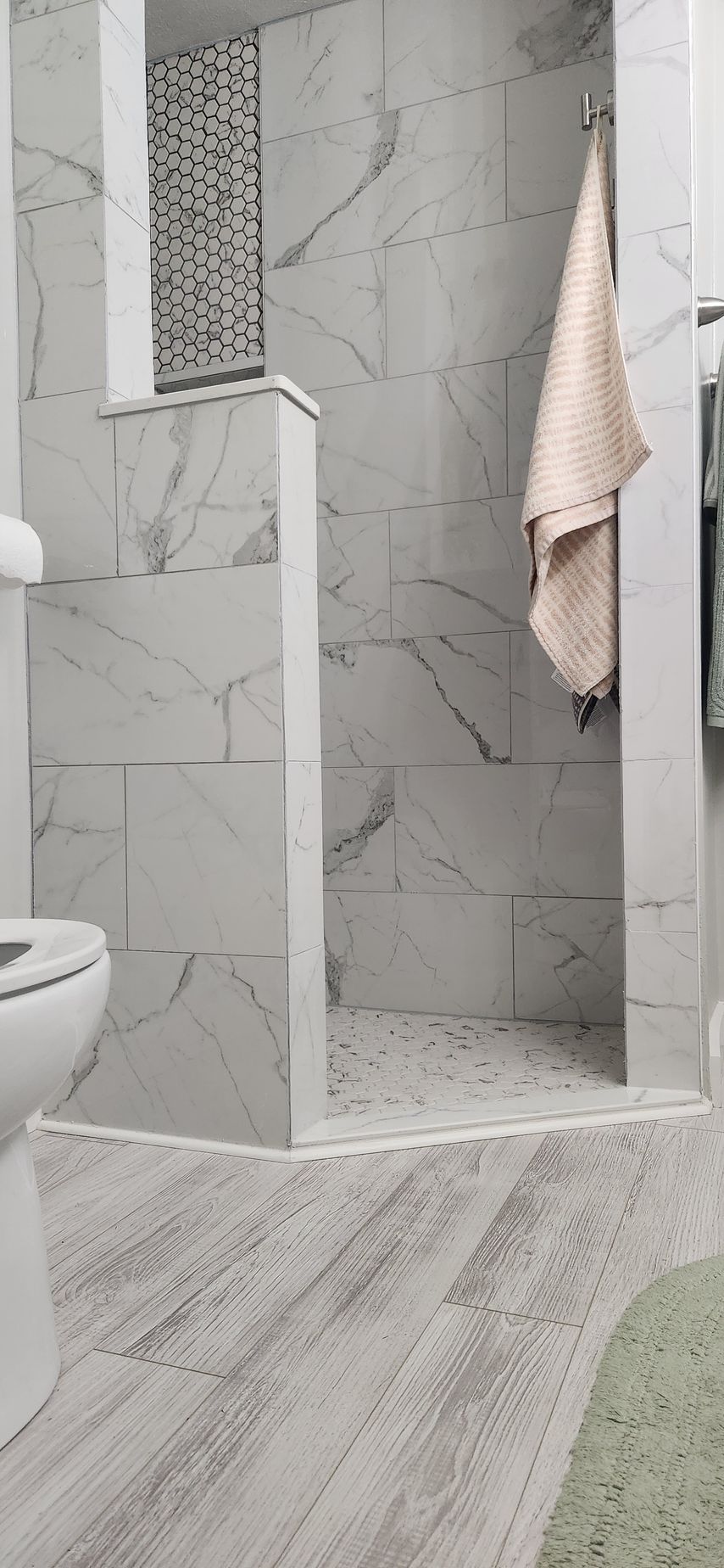 A modern bathroom with marble tile and a walk-in shower. A towel hangs in the shower. A toilet is in the foreground.