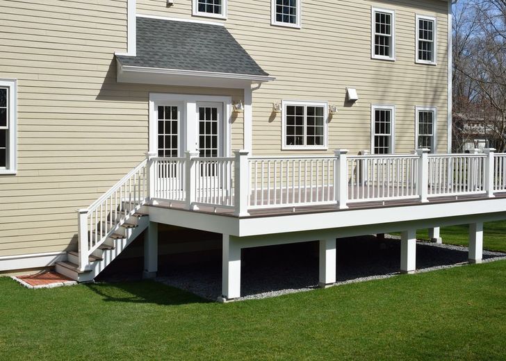 Back of a two-story beige house with a white deck, stairs, and French doors leading to the backyard.