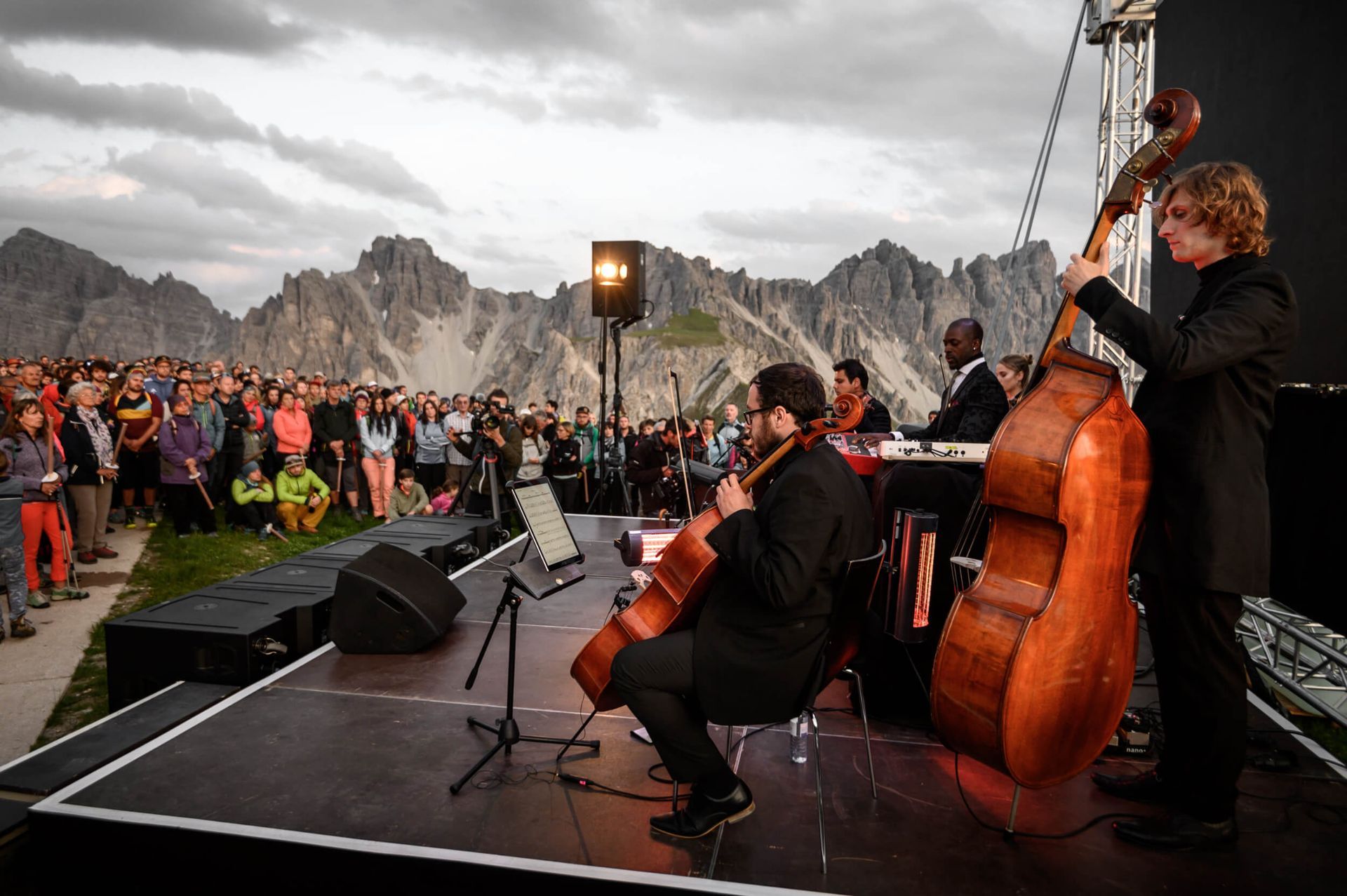 Jazz band performing outdoors on stage, audience watching. Mountains in background.