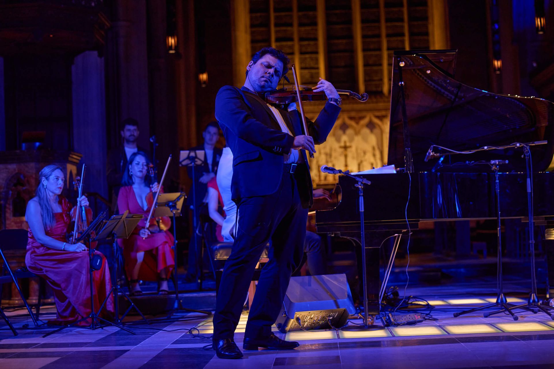 Man playing violin in an orchestra, in a hall with blue light.