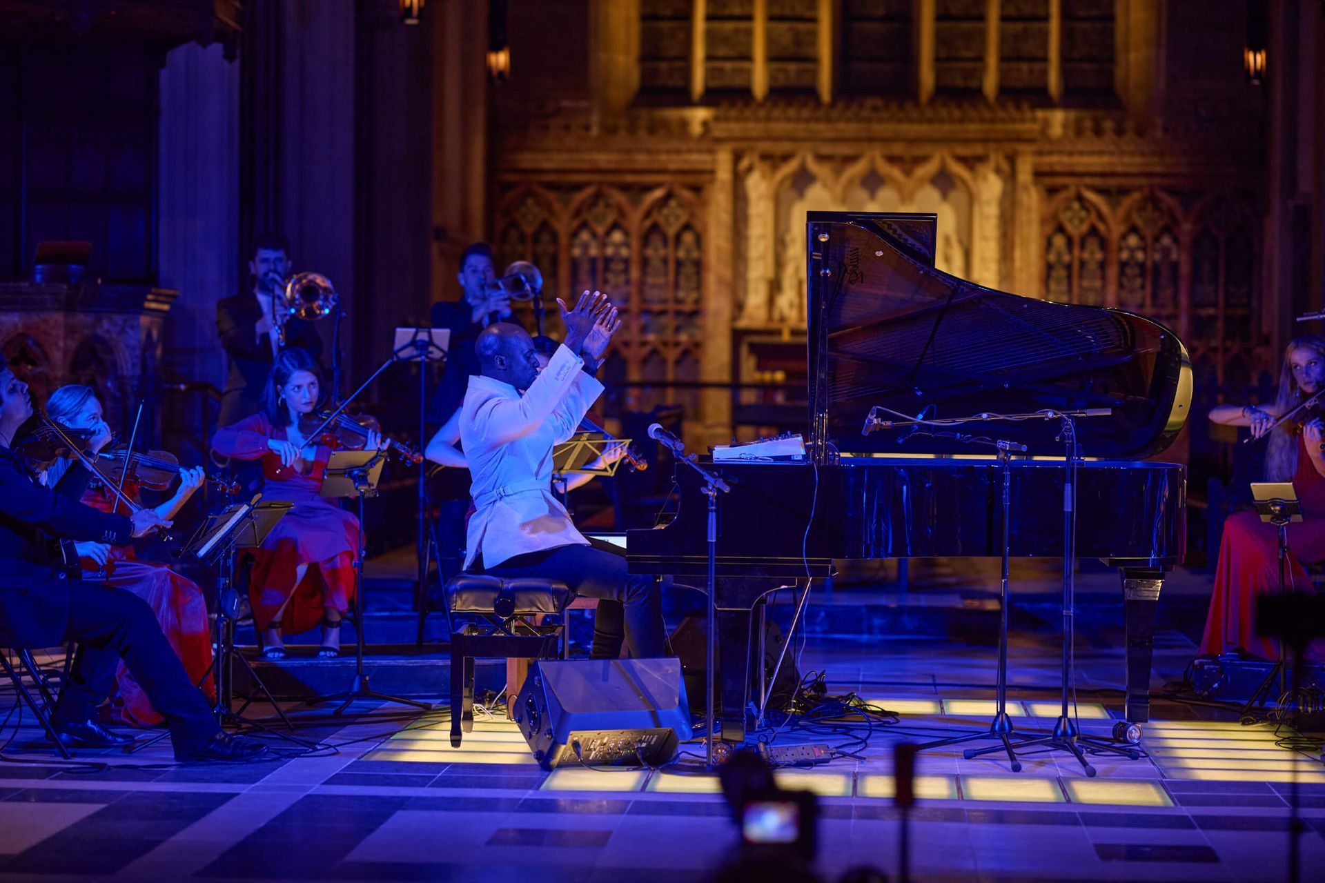 Pianist performing on stage with an orchestra in a church. Blue and warm lighting.