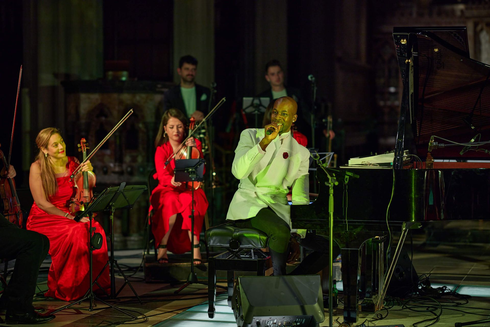 Singer in white suit performs with string and keyboard ensemble on stage.
