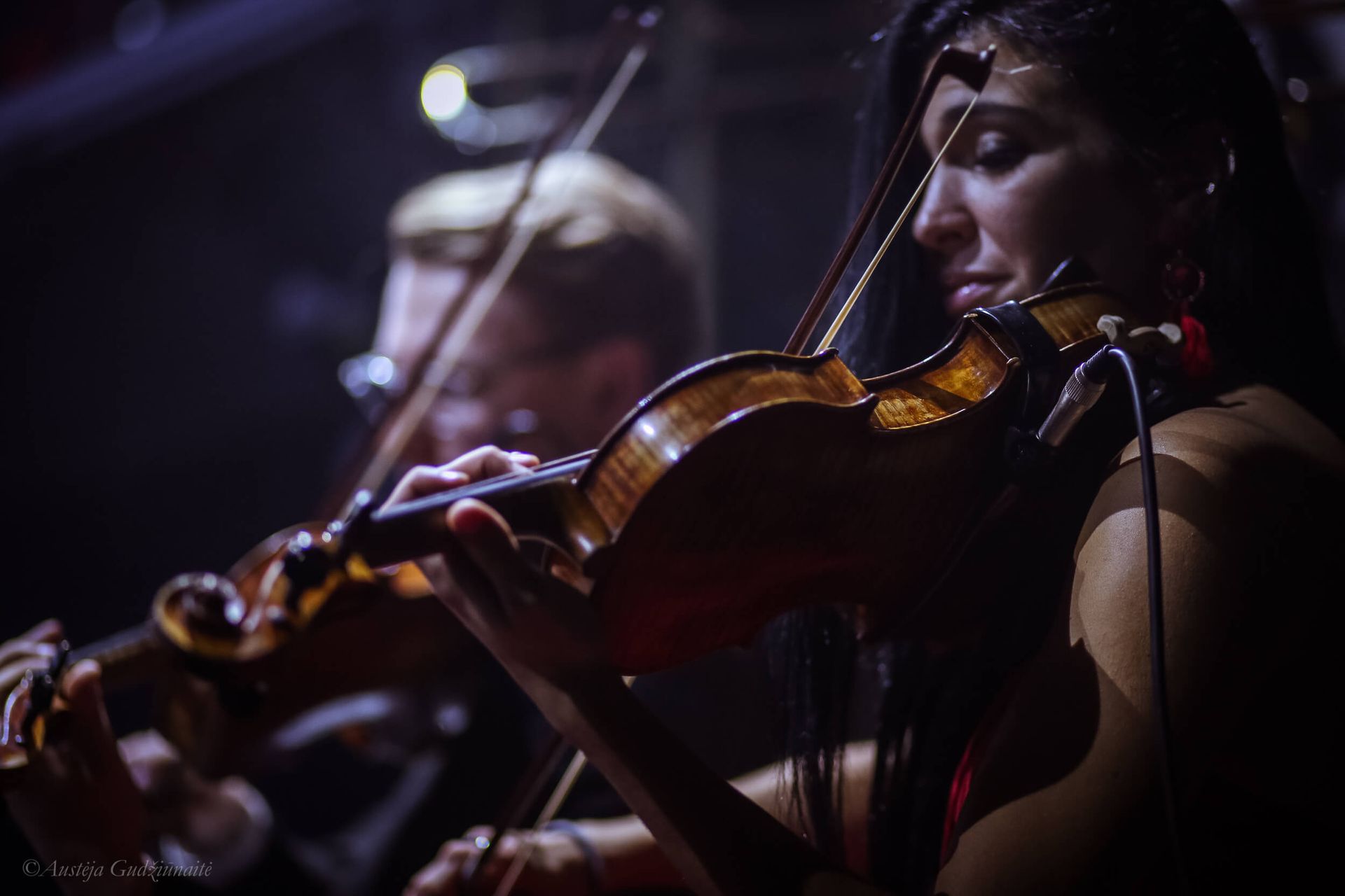 Two people playing violins on a dimly lit stage.