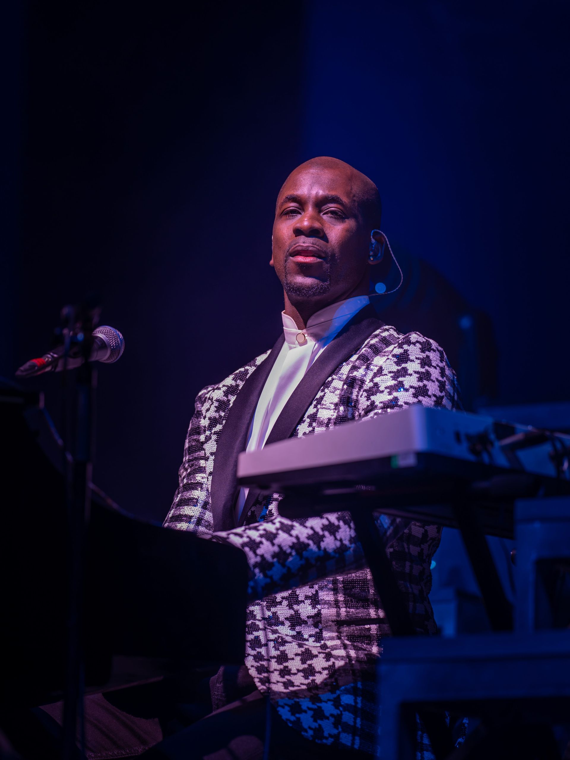 Man playing keyboard on stage wearing black and white patterned suit jacket.