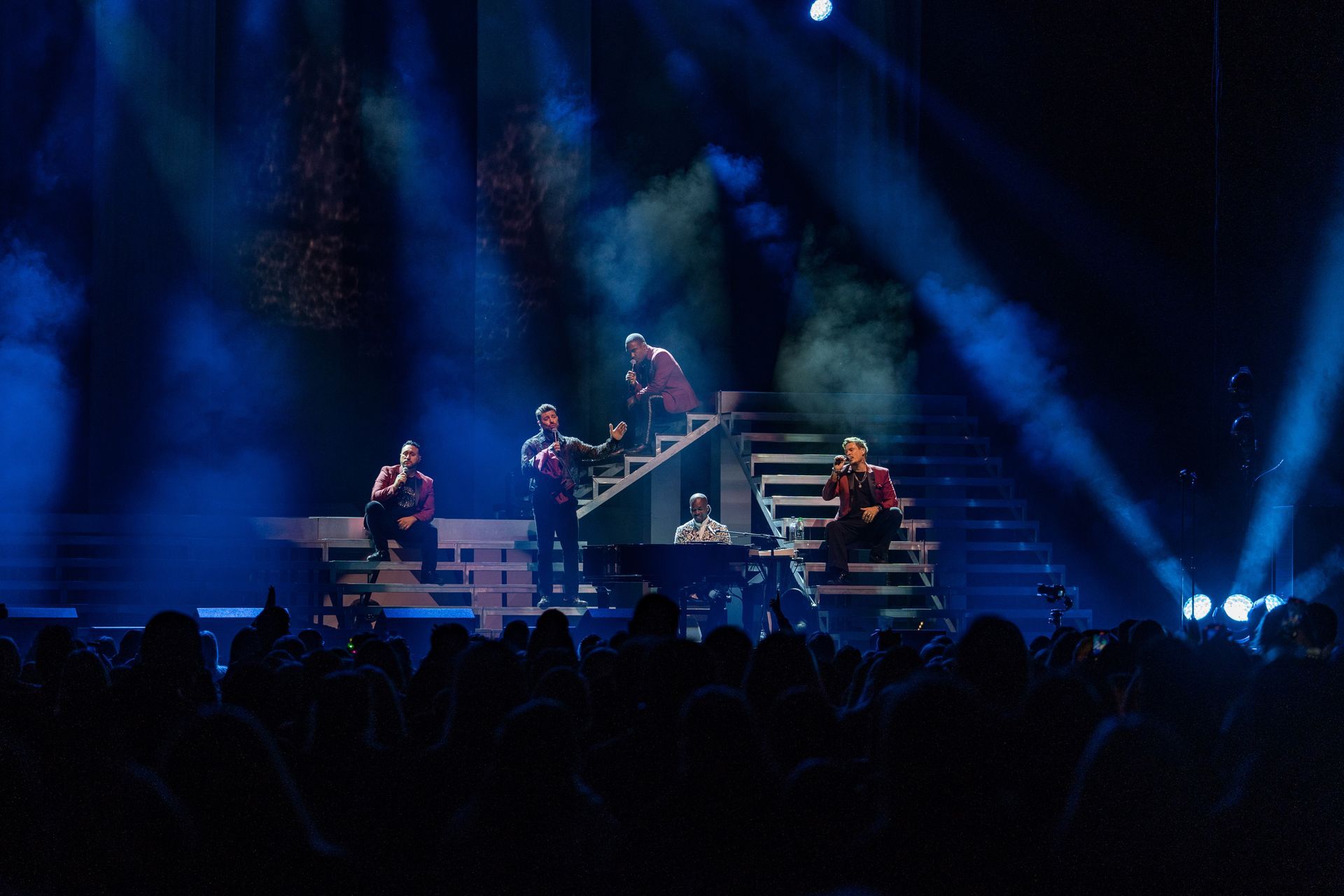 Band performs on stage under blue spotlights, crowd in foreground.
